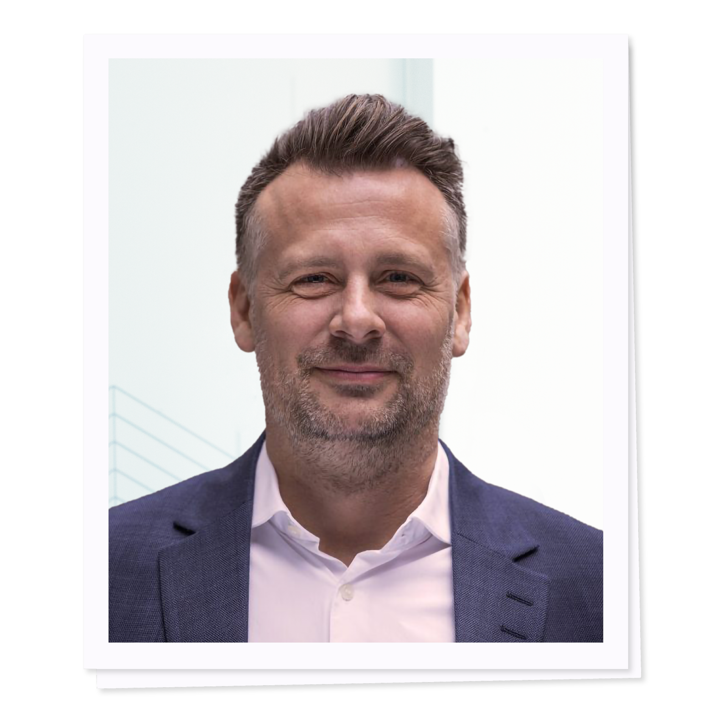 Man in a suit with short hair and slight smile standing against a light background.