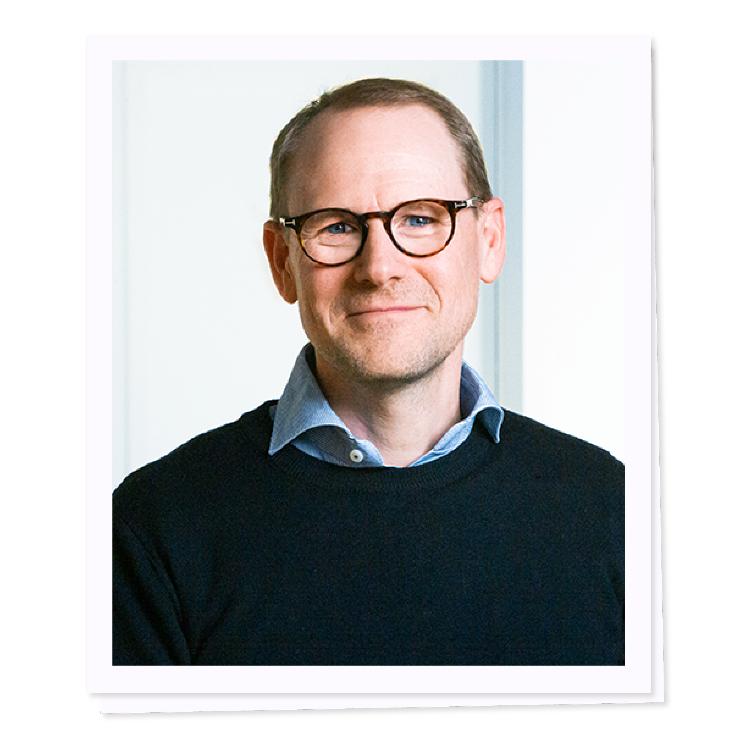 Man with glasses wearing a blue shirt and sweater, smiling.