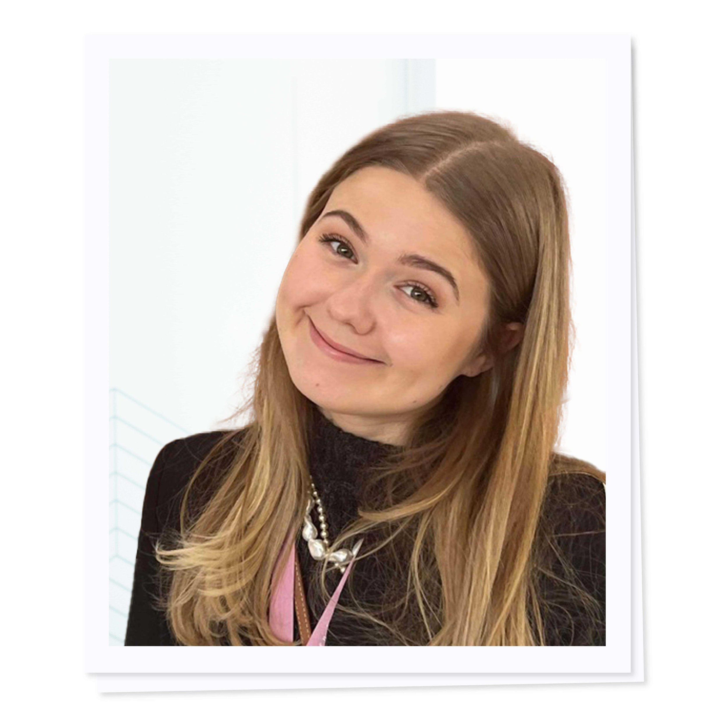 Smiling woman with long hair, wearing a black top and a necklace, against a white background