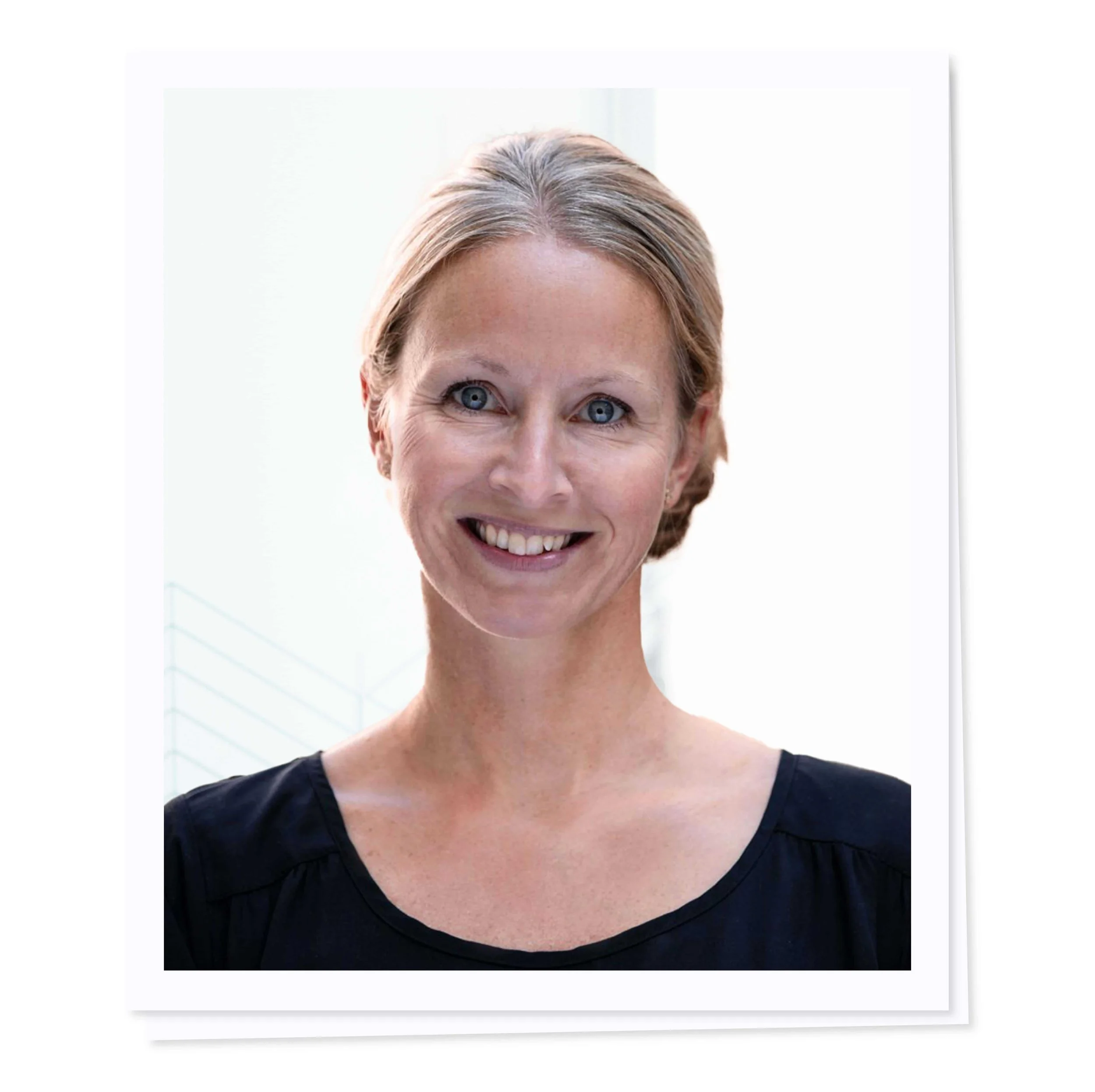 Smiling woman with light brown hair tied back, wearing a black top against a light background.