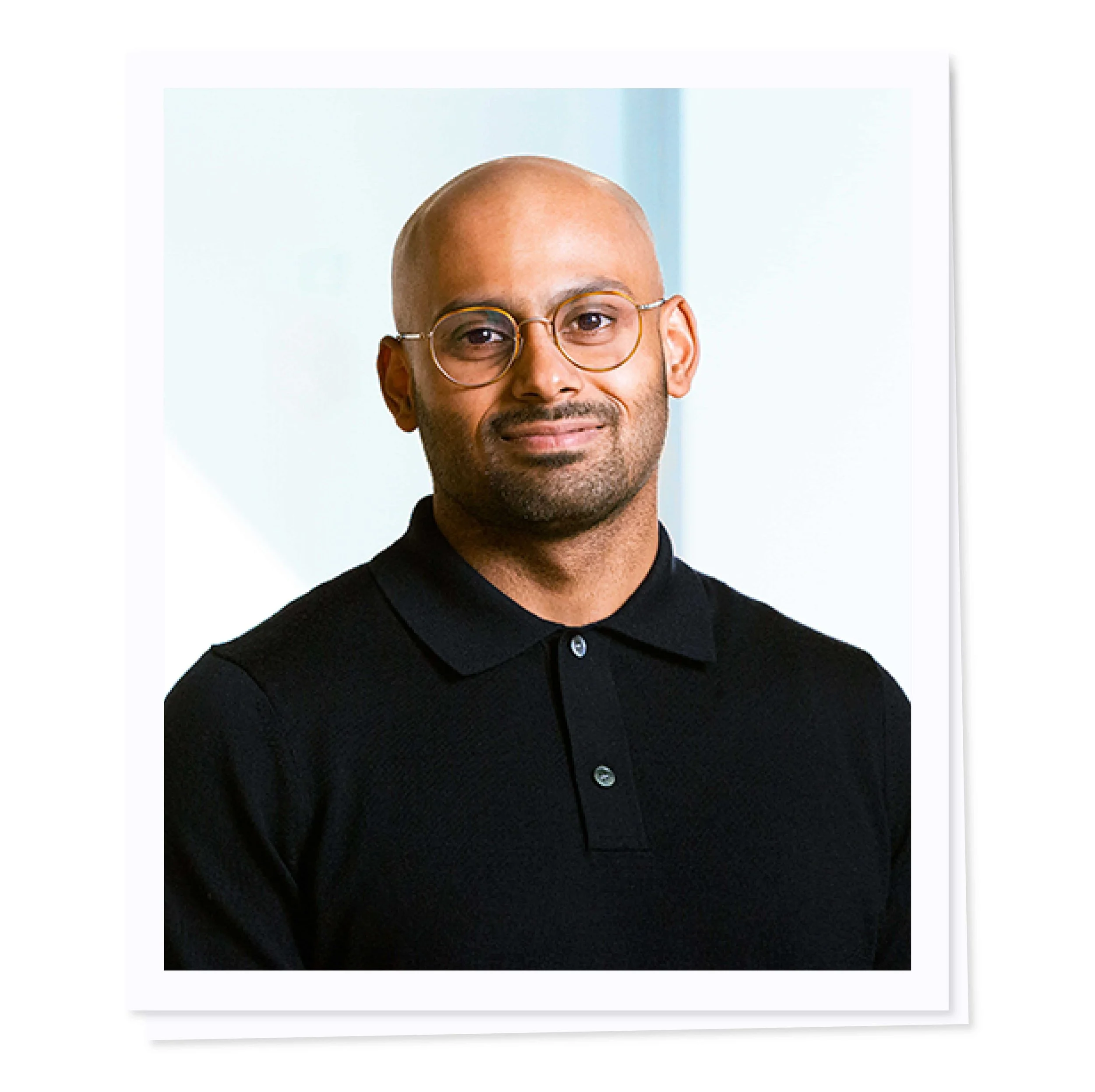 Man wearing glasses and a black shirt, smiling slightly, on a light background.
