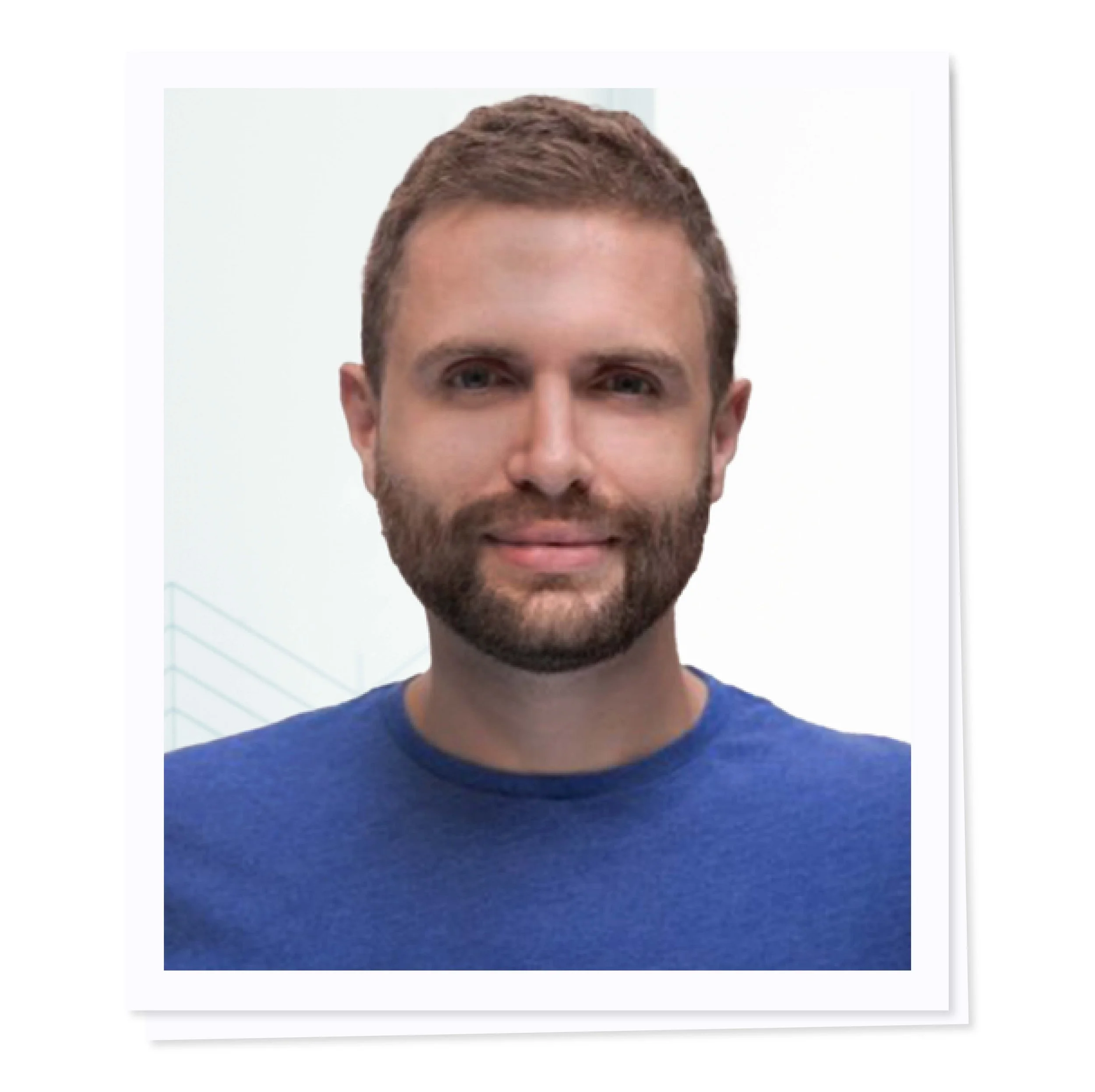 A man with a beard wearing a blue shirt, smiling against a white background.
