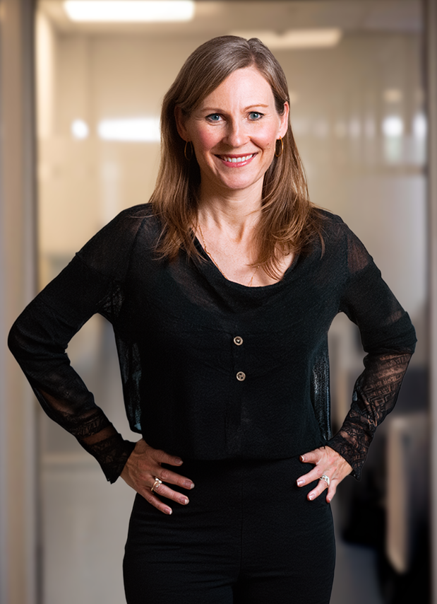 Woman smiling in a black top with hands on hips in a bright room.