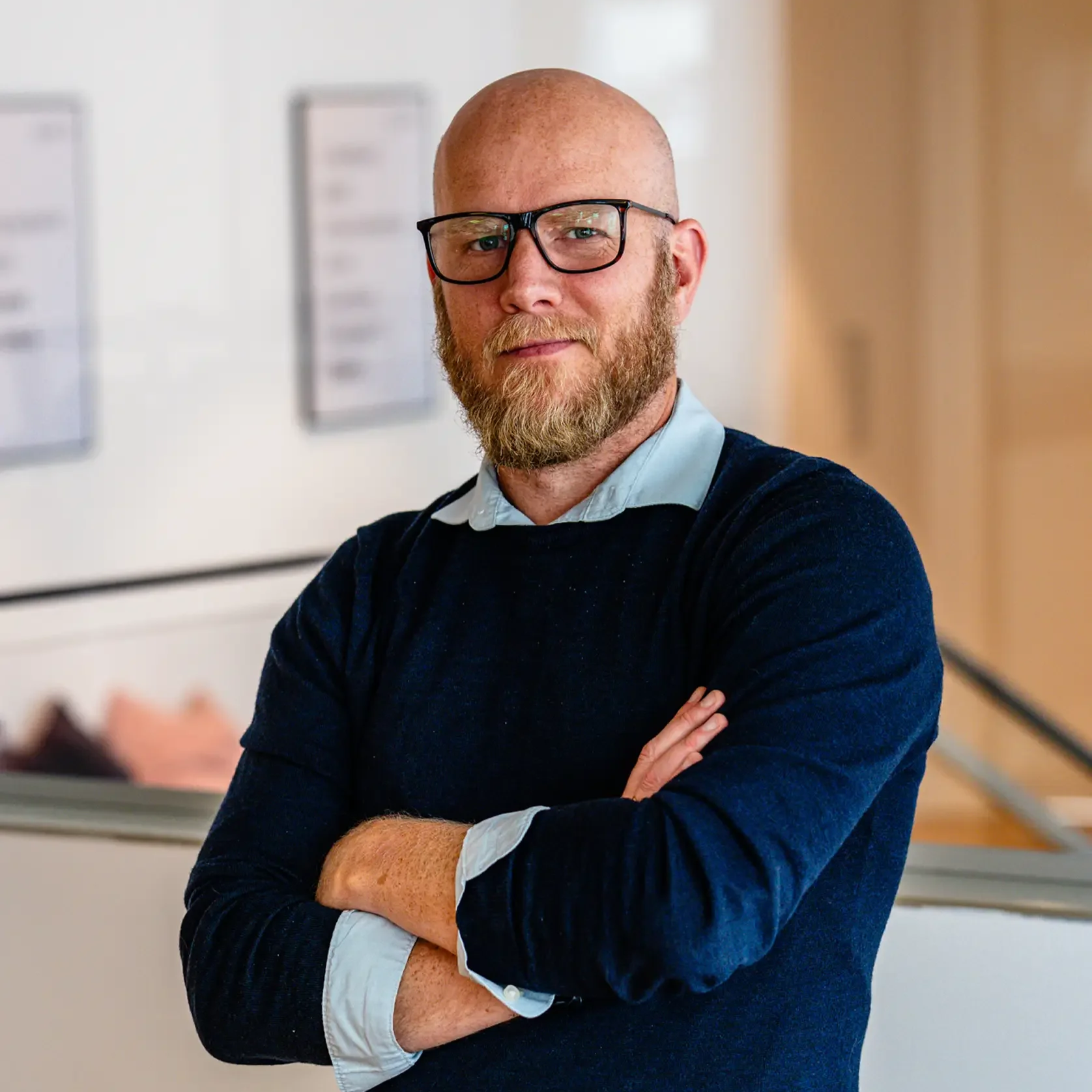 Bald man with a beard wearing a suit and light blue shirt, facing forward against a light background.