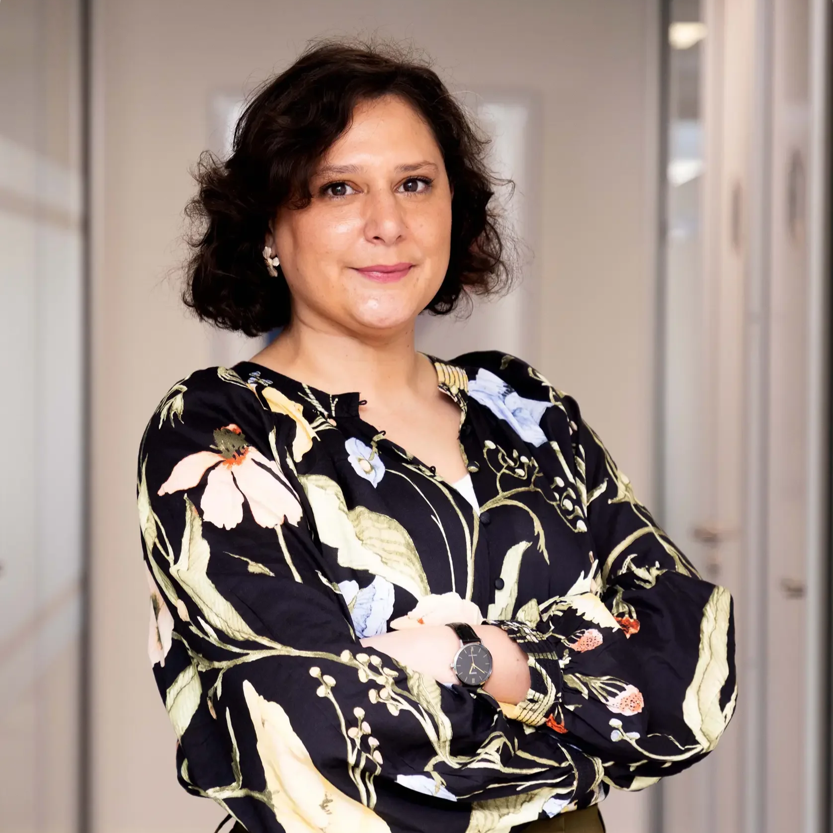 Person wearing a polka dot blouse standing indoors with a neutral expression.