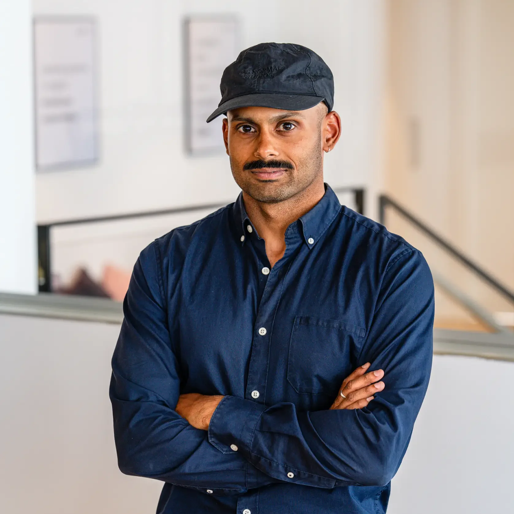 A person with glasses wearing a black shirt, standing against a light background.