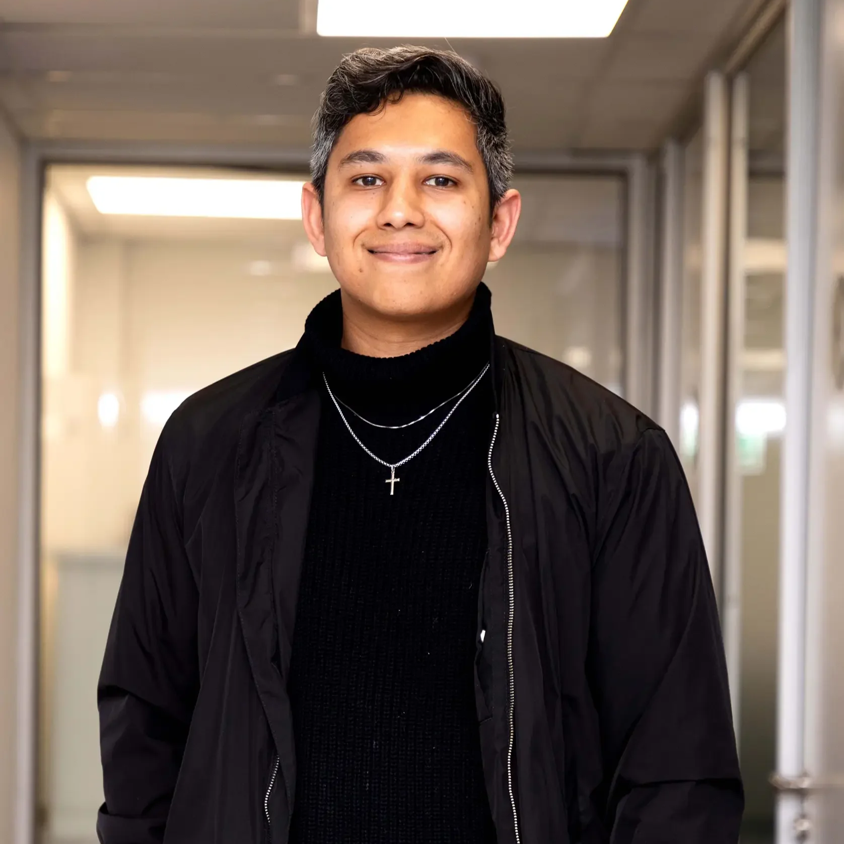 Smiling man in white button-up shirt, arms crossed, standing against a light background.