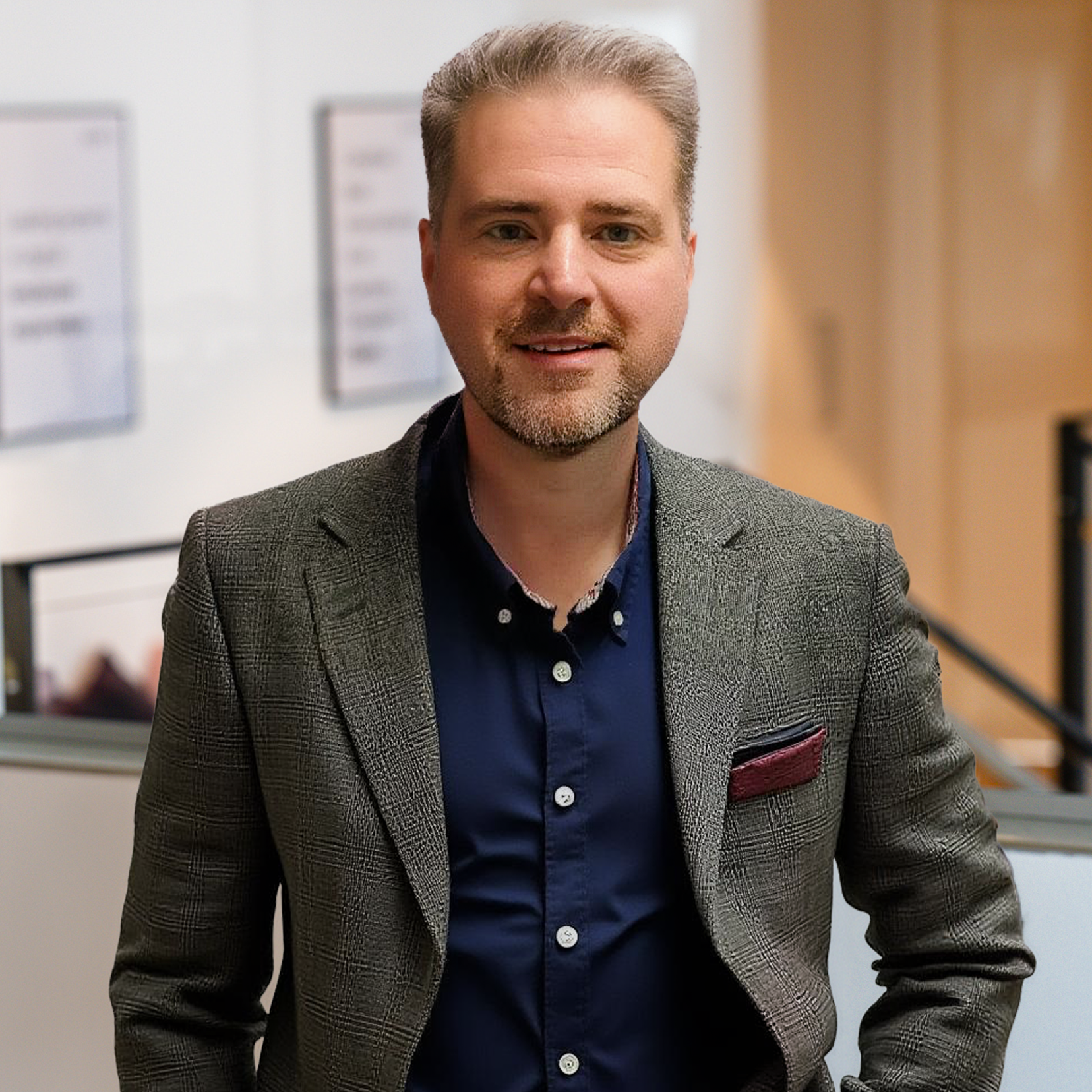 A smiling man in a gray blazer and navy shirt with a light beard.