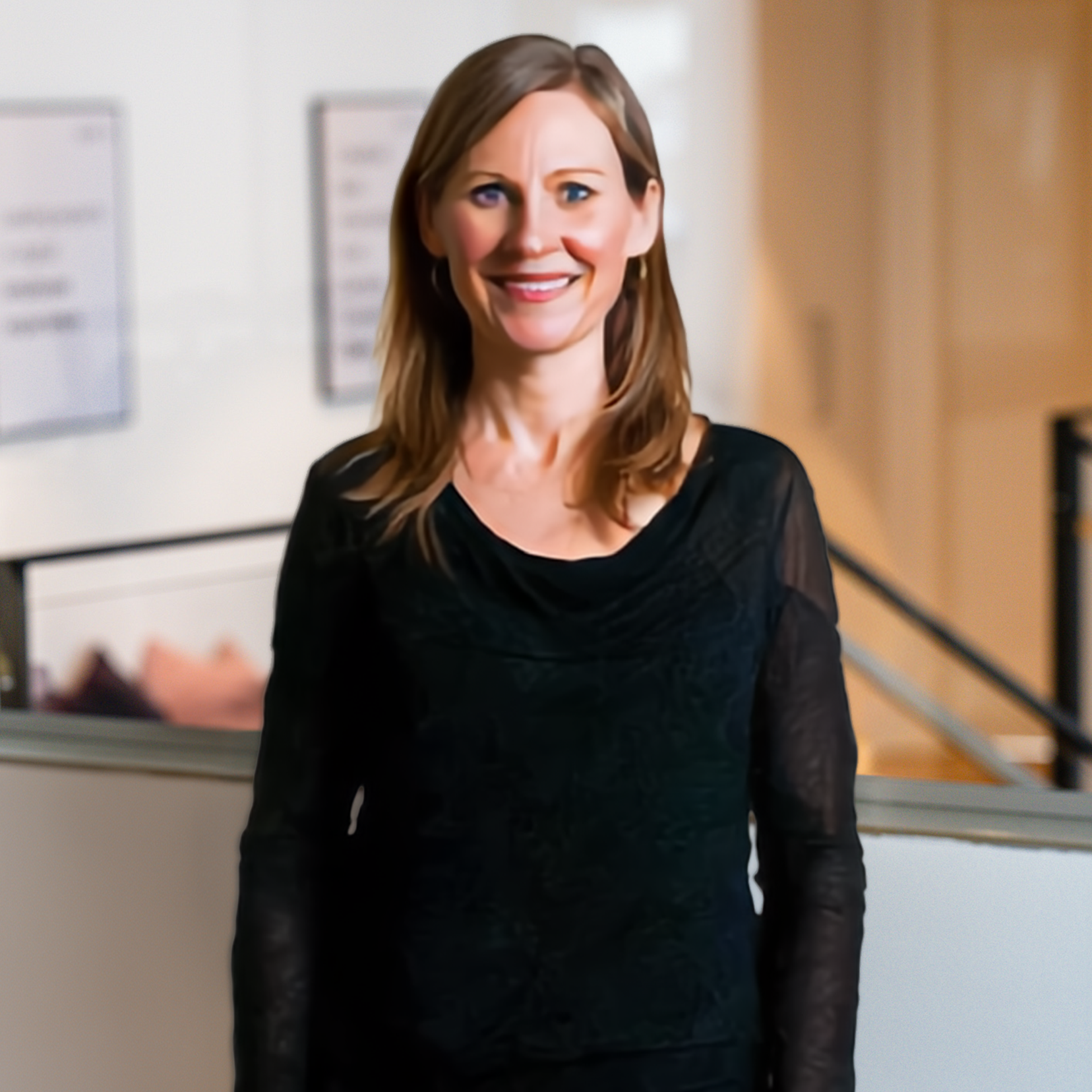Woman smiling in a black top with hands on hips in a bright room.