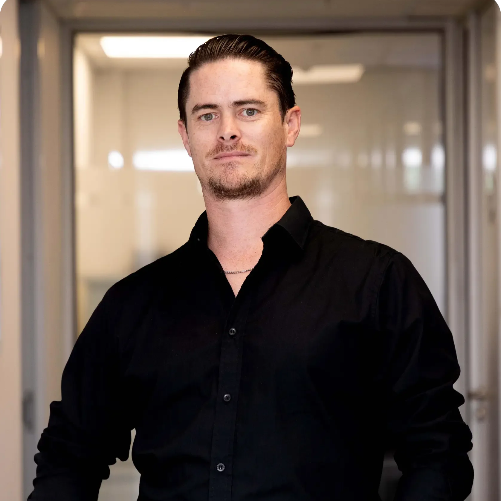 Man in a plaid shirt with short hair, standing against a light background with geometric patterns.
