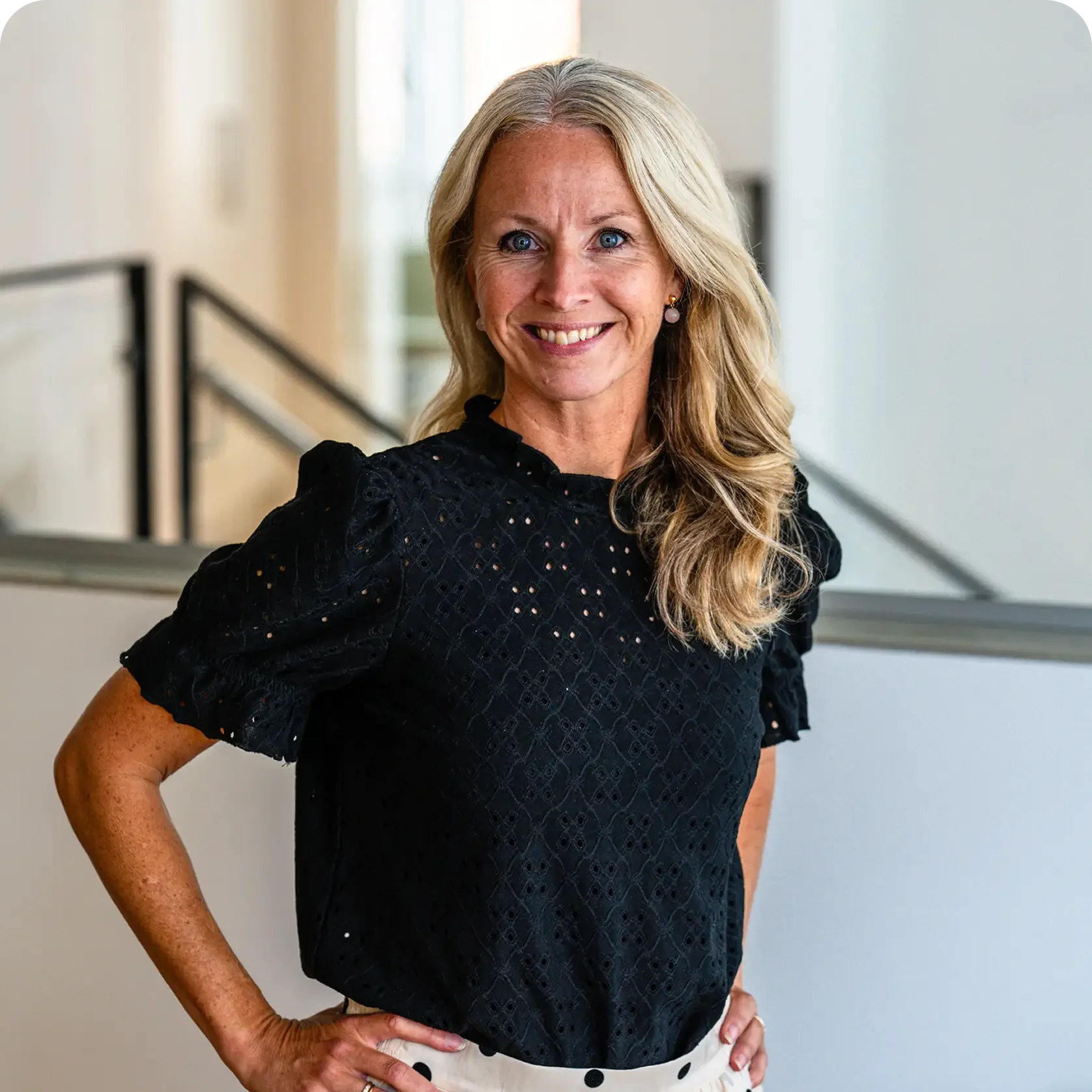 Smiling person with light hair pulled back, wearing a black top, against a light background.