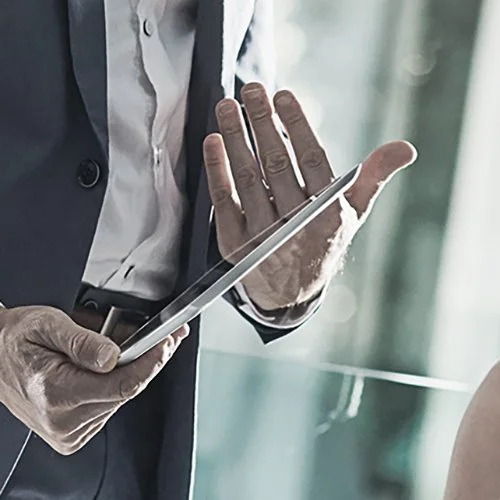 Close-up of a person in a business suit using a tablet, with their hand raised as if to stop or signal approval.