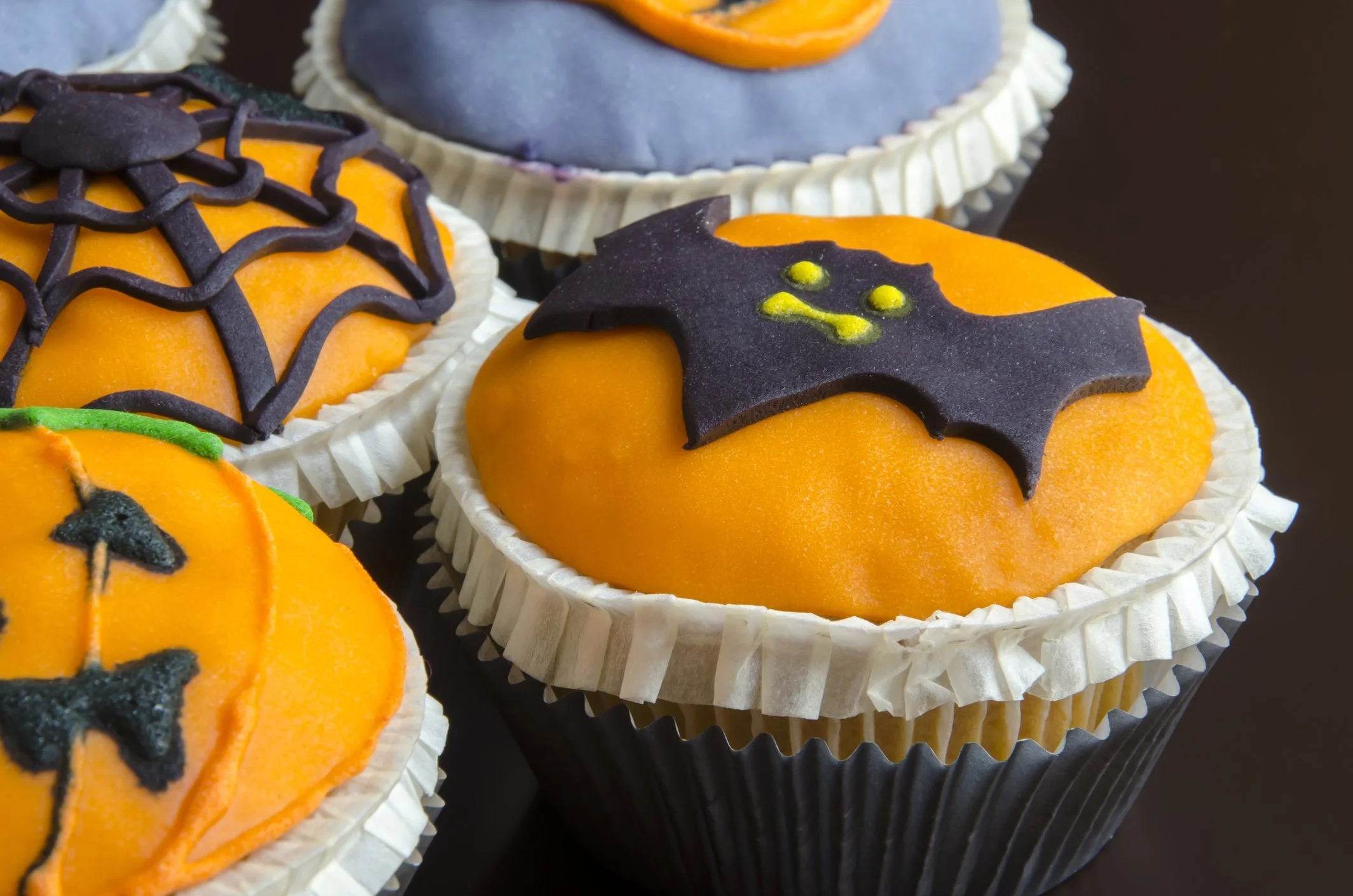 Cupcake décoré avec une tête de fantôme de Halloween, avec des yeux, un nez et une bouche en chocolat, tenu entre deux mains.