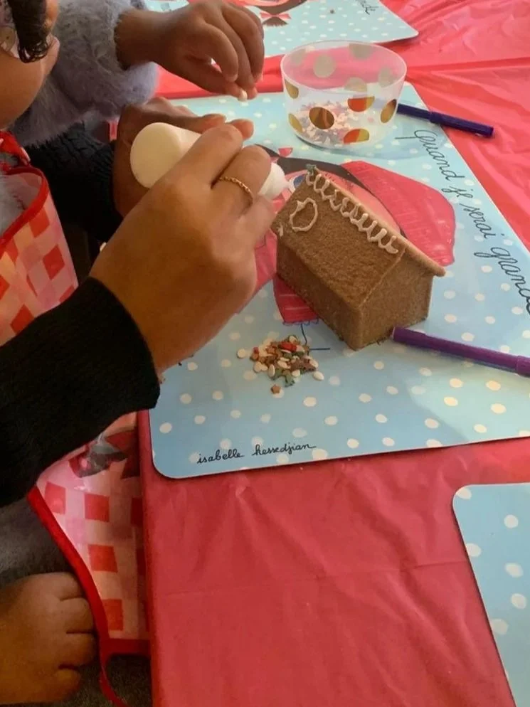 Deux jeunes filles décorent un gâteau de Noël lors d'une fête. Elles portent un bonnet de fête et un tablier rouge, avec des décorations de Noël sur la table.