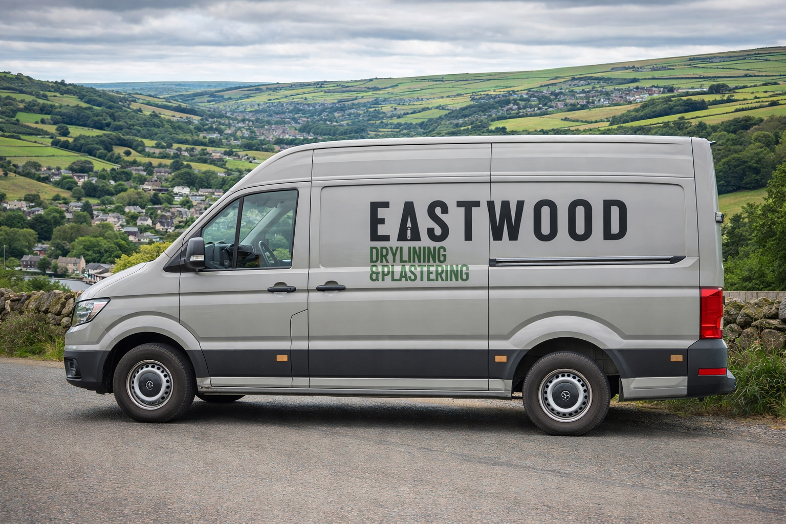Gray work van with 'EASTWOOD DRYLINING & PLASTERING' logo parked on a road with a scenic view of green hills and a village in the background.