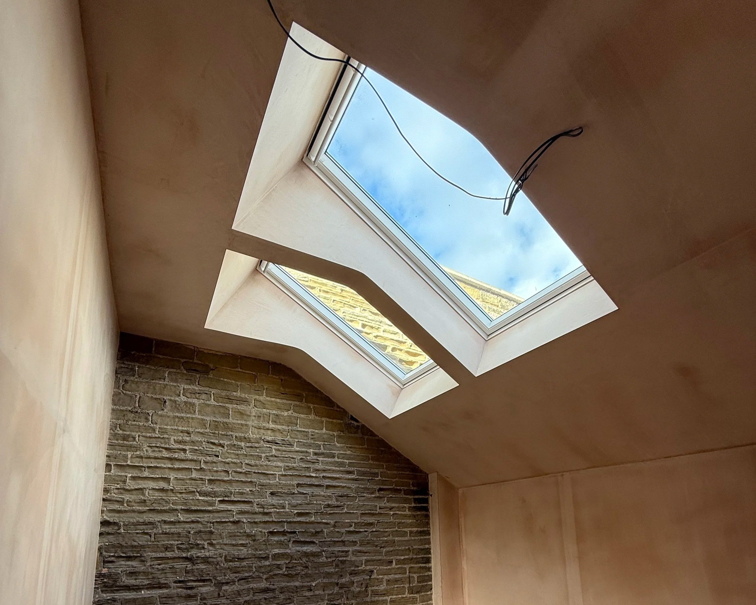 Interior view of a room with a skylight window showing a blue sky with clouds and part of a brick wall.