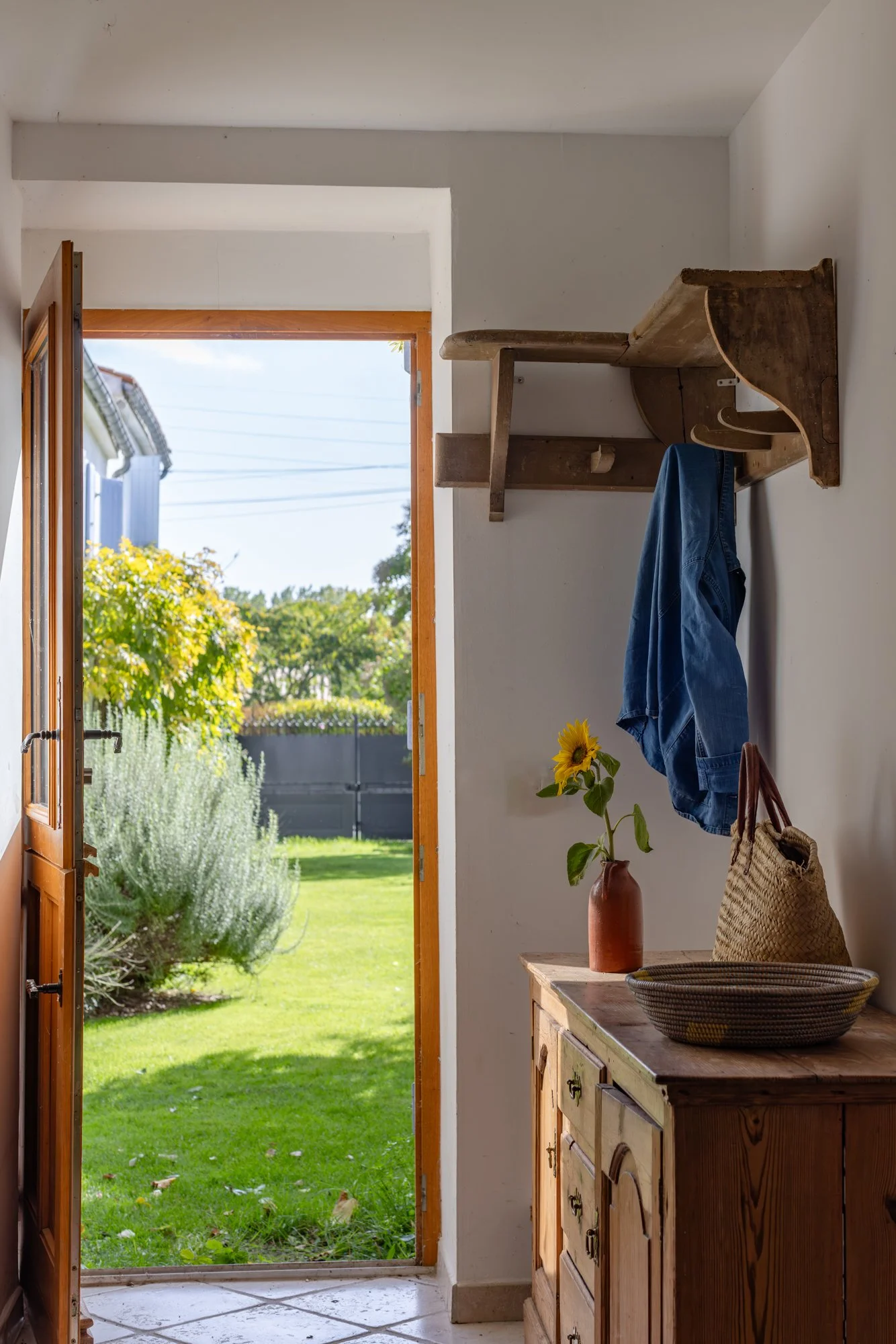 A view from inside a house looking out through an open wooden door to a green outdoor garden with trees and plants.
