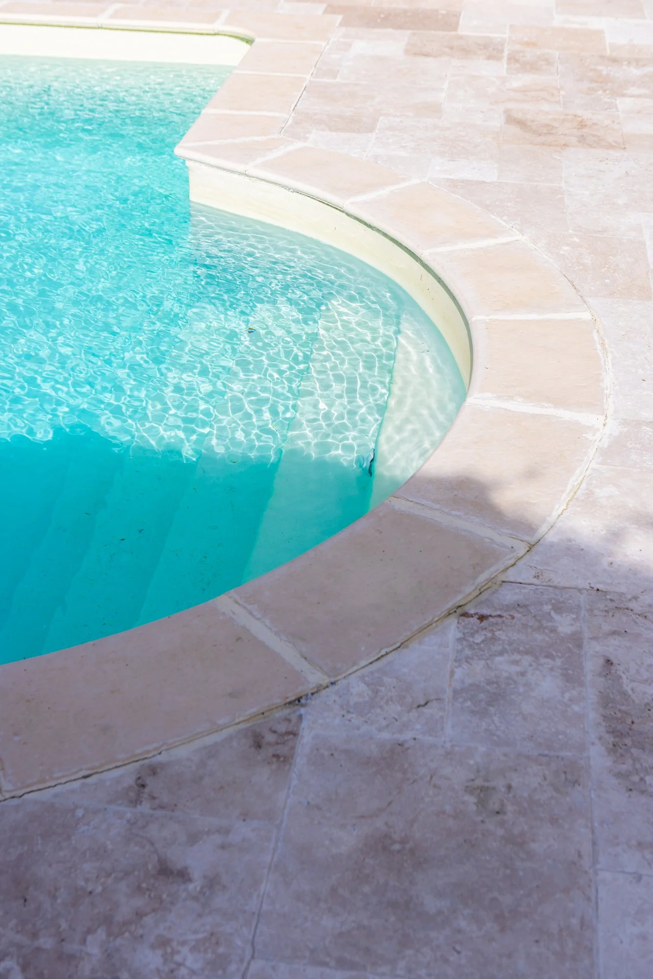 Close-up view of a swimming pool with clear blue water and a tiled beige pool deck surrounding it.