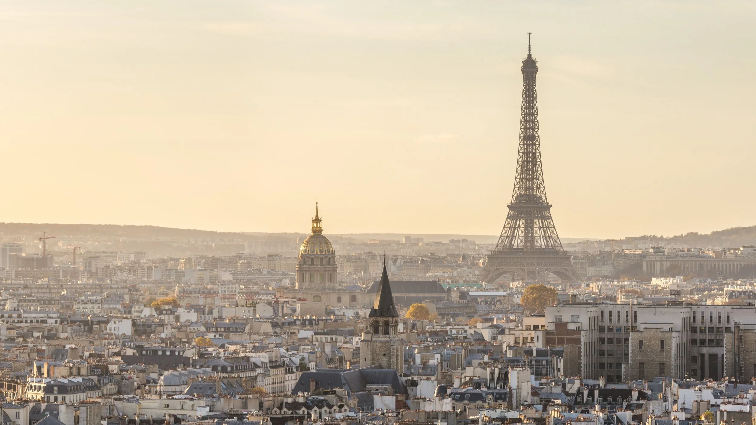 Panoramic view of Paris featuring the Eiffel Tower, golden-domed Invalides, and historic buildings with gray rooftops during daytime with clear sky.