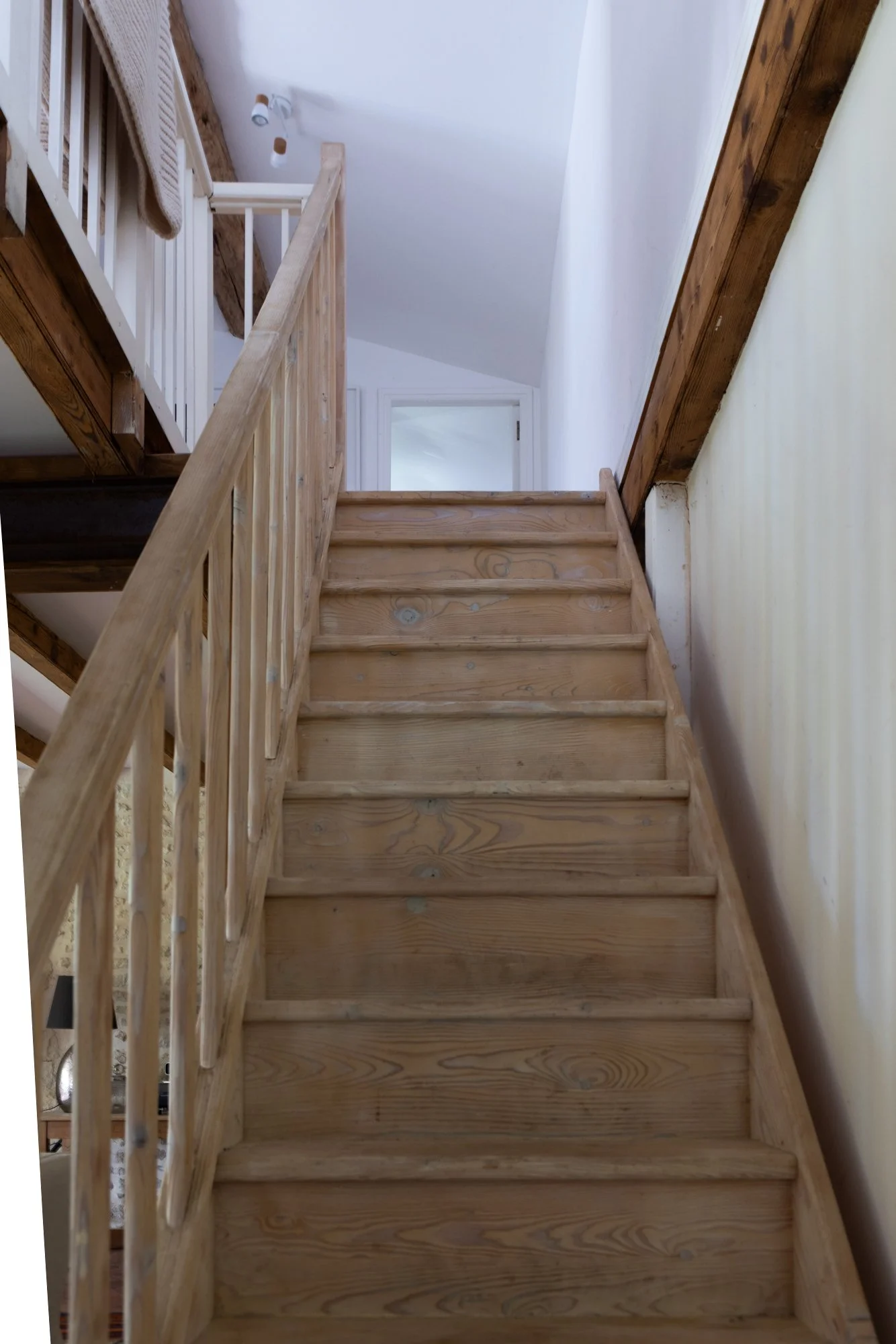 Wooden staircase in a home with a railing on one side, leading up to a landing near a doorway.