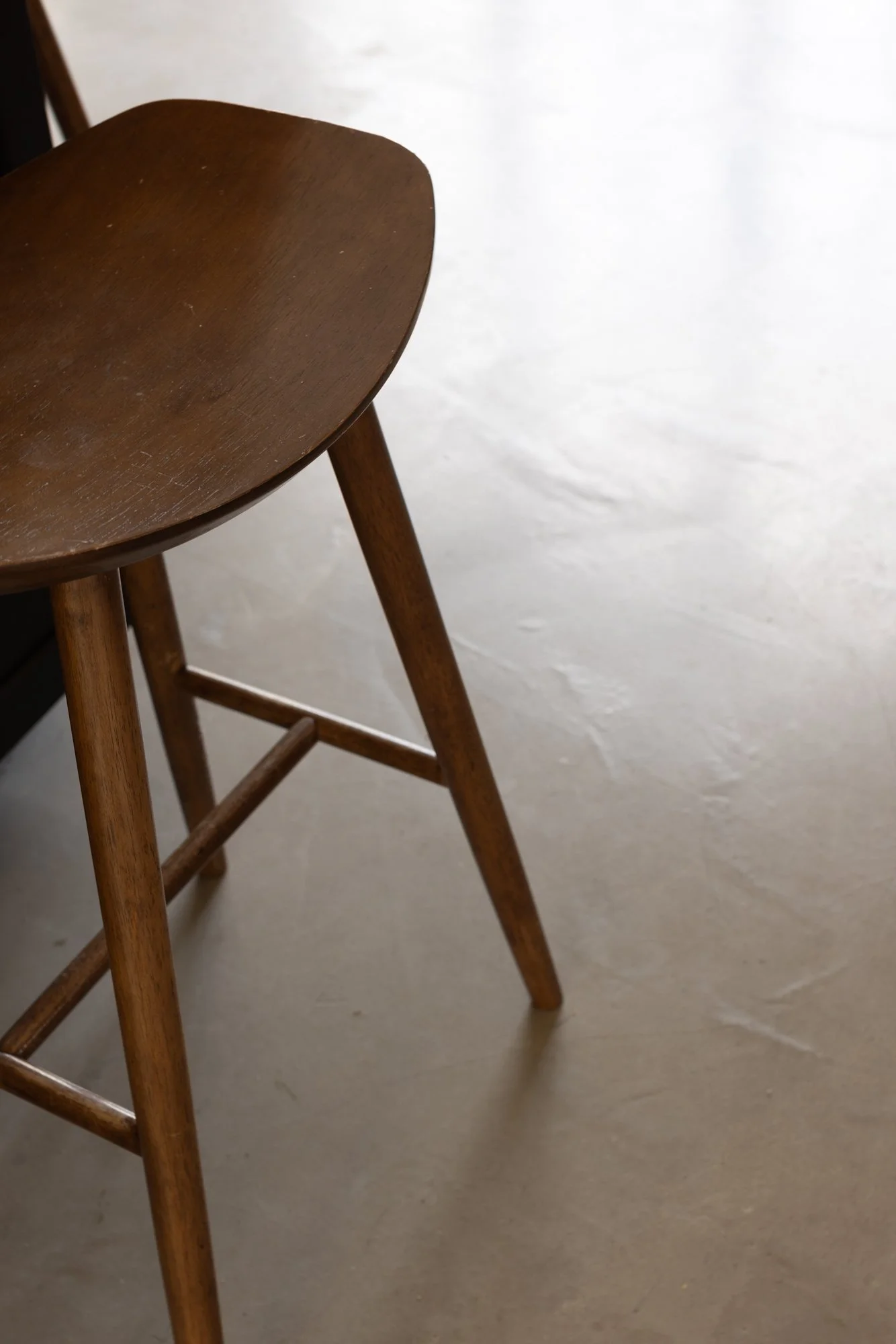 A wooden chair with a curved seat and four legs, situated on a plain, light-colored floor.