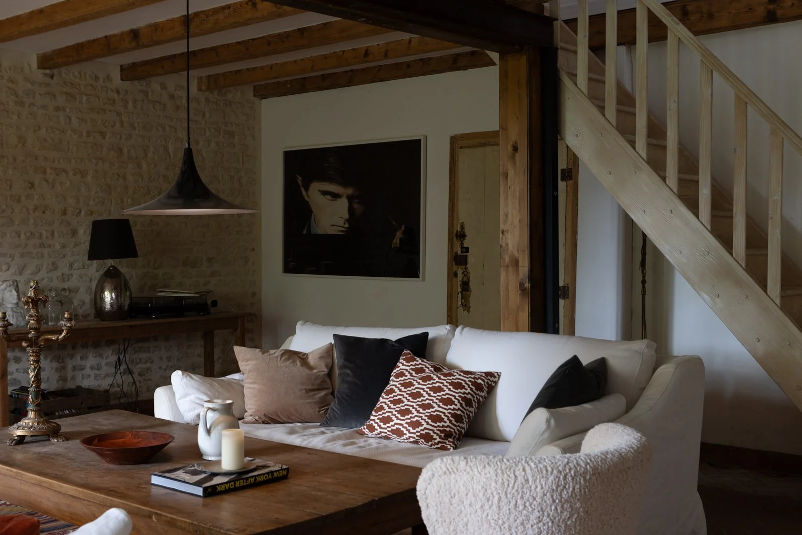 Living room with a white sofa, decorative pillows, wooden coffee table, stone wall, staircase, and large framed photo of a man on the wall.