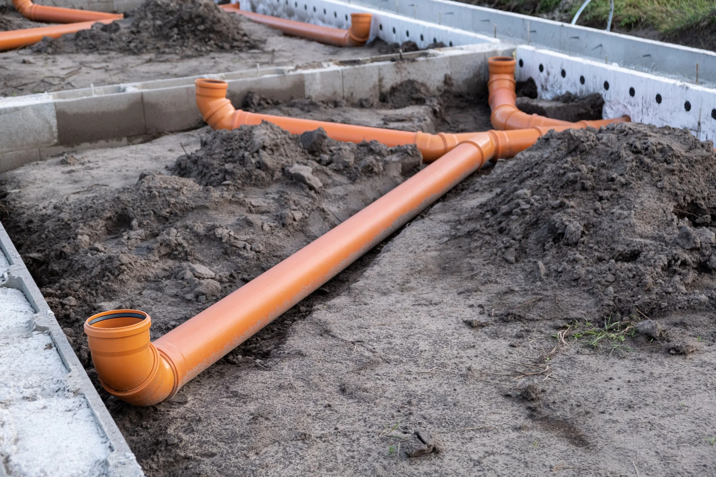 Construction site with orange PVC pipes and cinder blocks for plumbing installation.