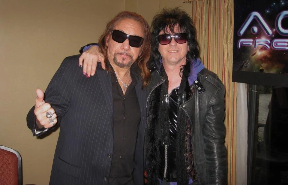 Digital artist, Concert lighting director, writer Woody Bavota, Ace Frehley performing on stage, wearing sunglasses, with long hair and a patterned jacket, playing an electric guitar.