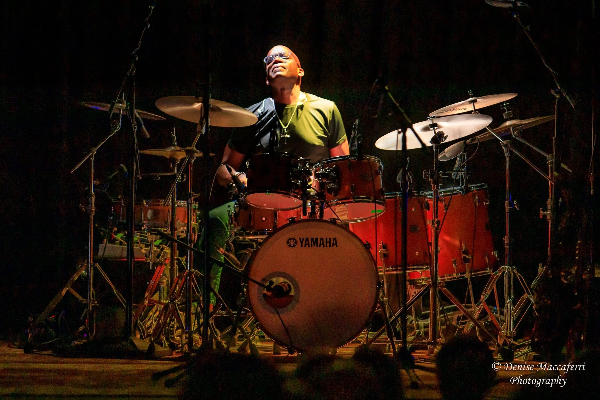 Digital artist, Concert lighting director, writer Woody Bavota, Spyro Gyra performing on stage with colorful lights, featuring a saxophonist, keyboardist, bassist, drummer, and guitarist, in a venue with wooden accents and arched windows.