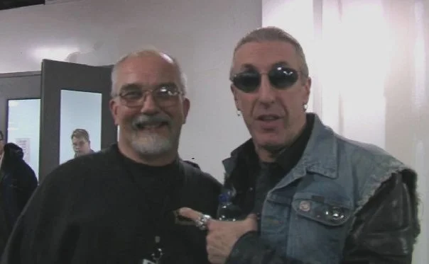 Two men posing for a photo indoors, with one wearing glasses and the other wearing sunglasses and a denim jacket.