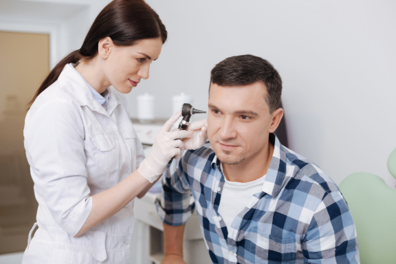 A healthcare professional using an otoscope on a man's ear in a clinical setting.
