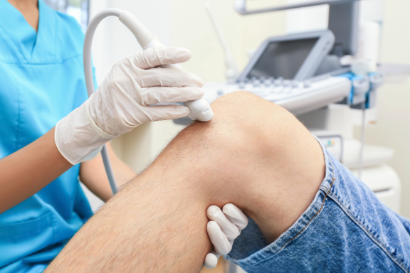 Medical professional performing an ultrasound on a patient's knee in a clinical setting.