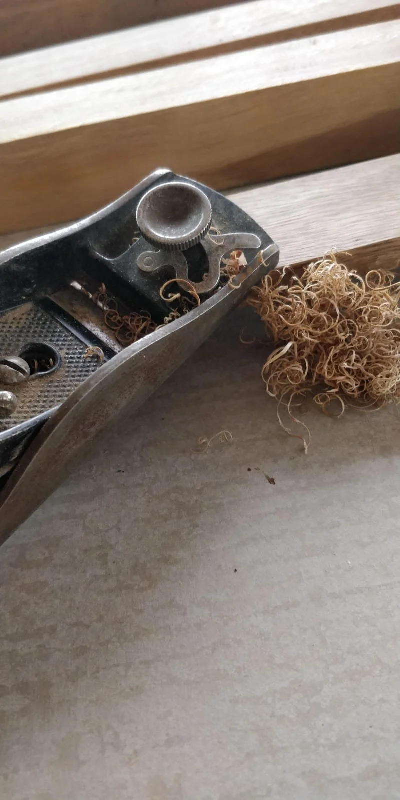 Close-up of a vintage hand plane, a woodworking tool, with wood shavings next to it on a gray surface.