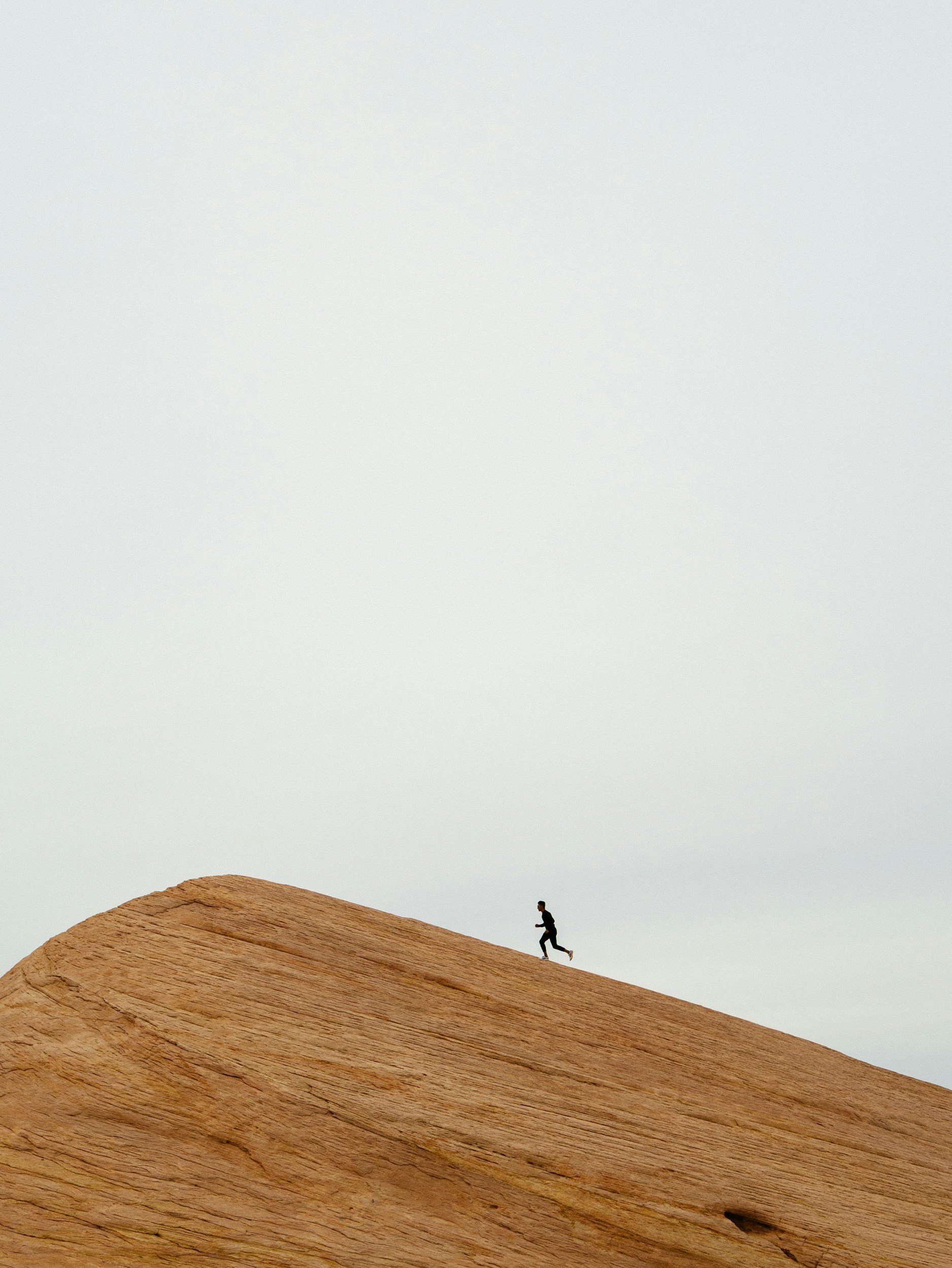 A small silhouetted person appears to be jogging on a large piece of wood or hill with a smooth inner curve, set against a plain, light background.