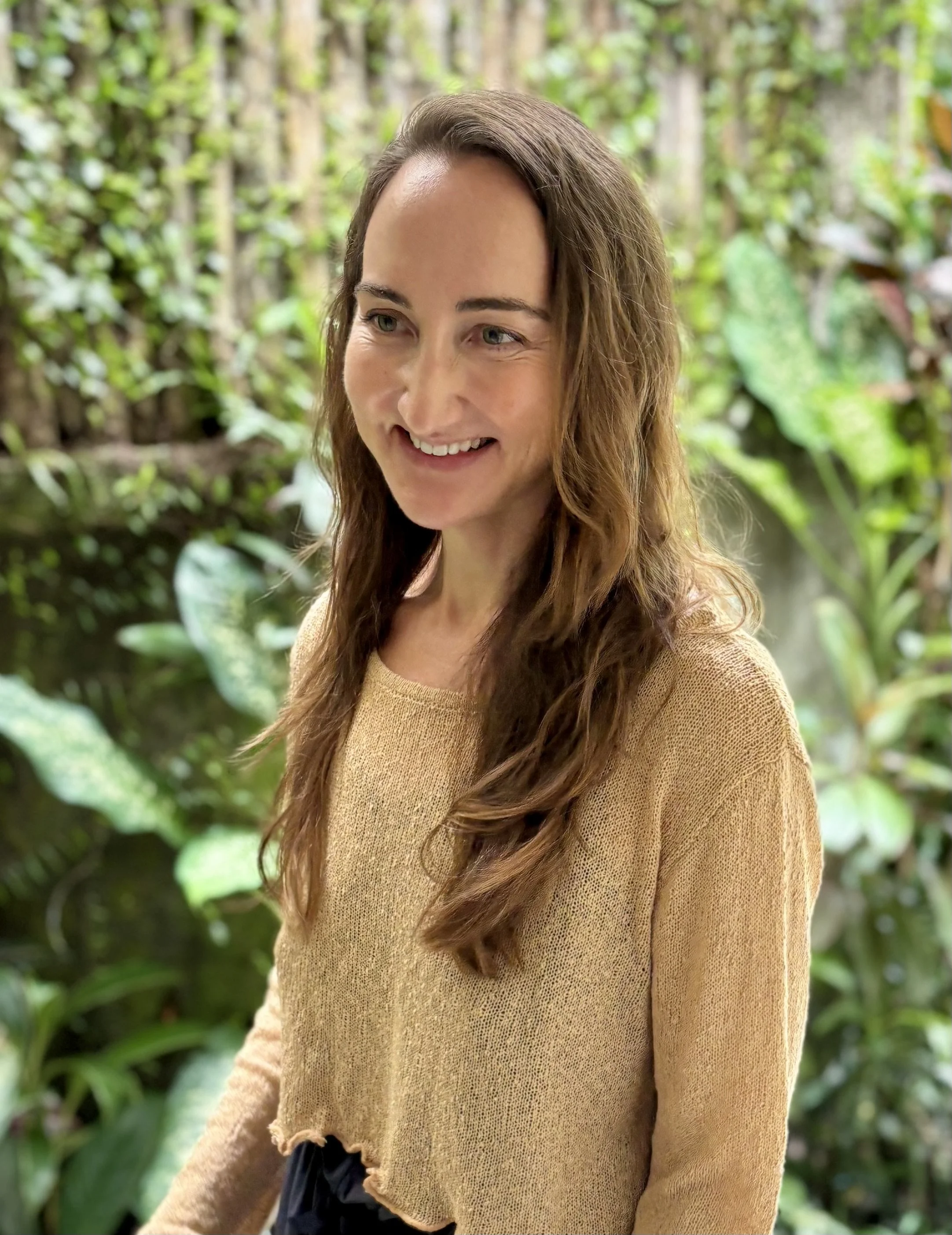 Licensed therapist with long brown hair smiling outdoors, standing in front of trees, About page image for an adult and couples therapy practice.