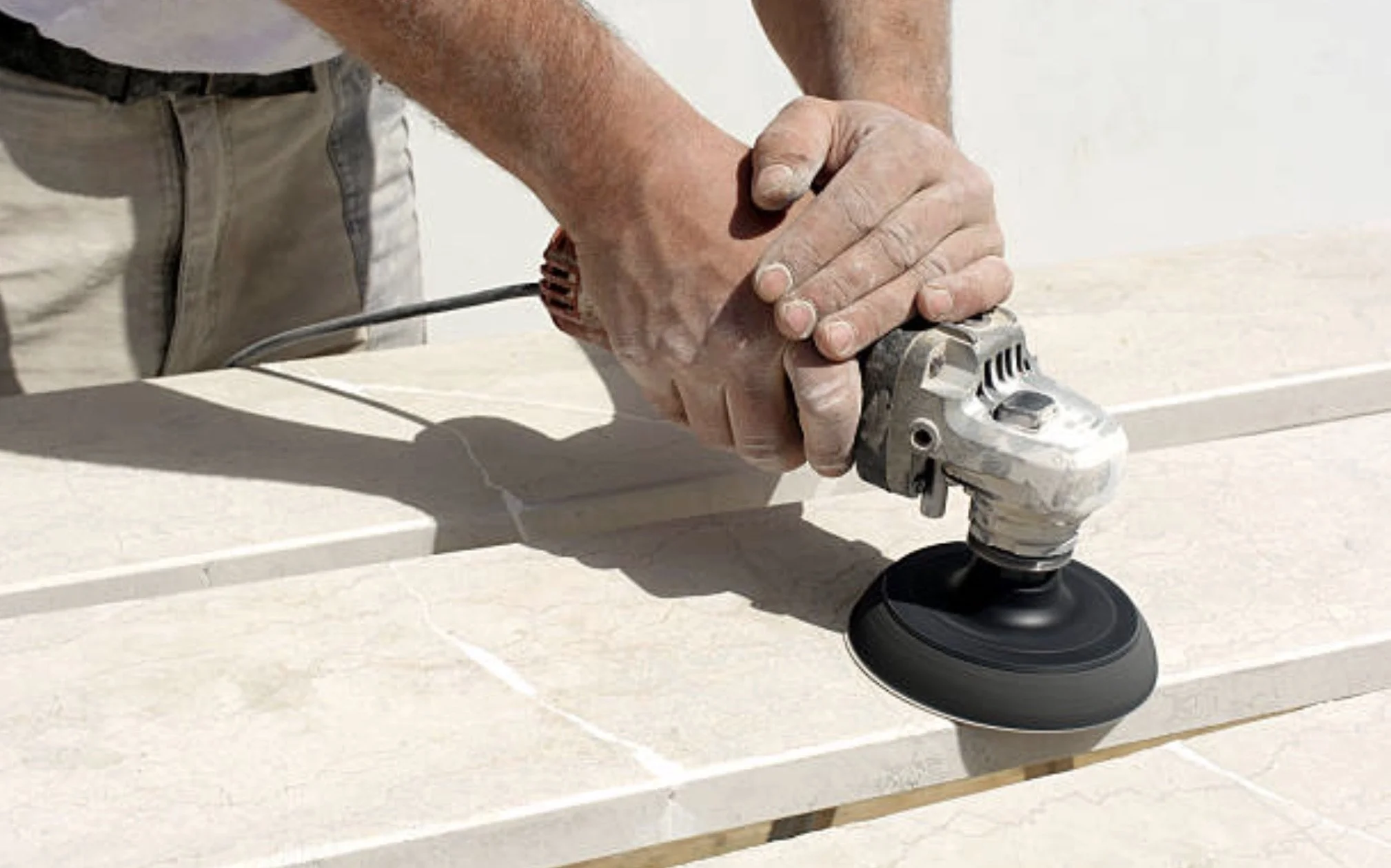 A person using a handheld power sander to polish a stone surface outdoors. ozstonestudio
