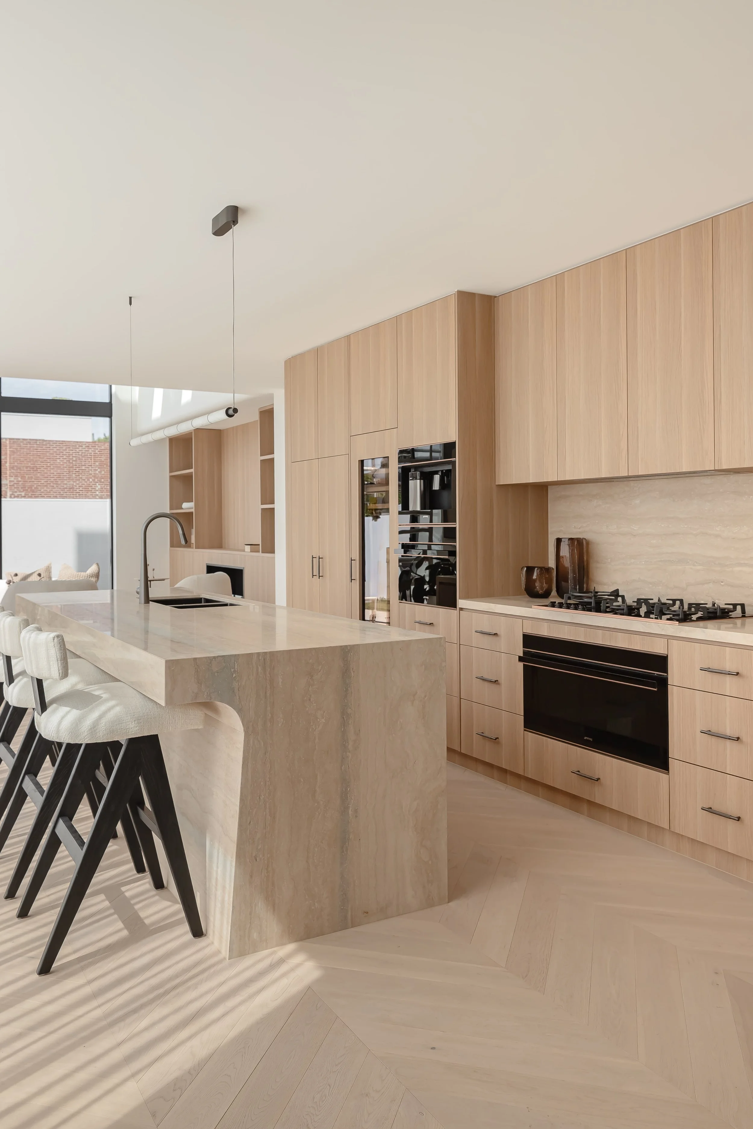Modern kitchen with beige wood cabinetry, a large island with a marble countertop, and built-in appliances.
