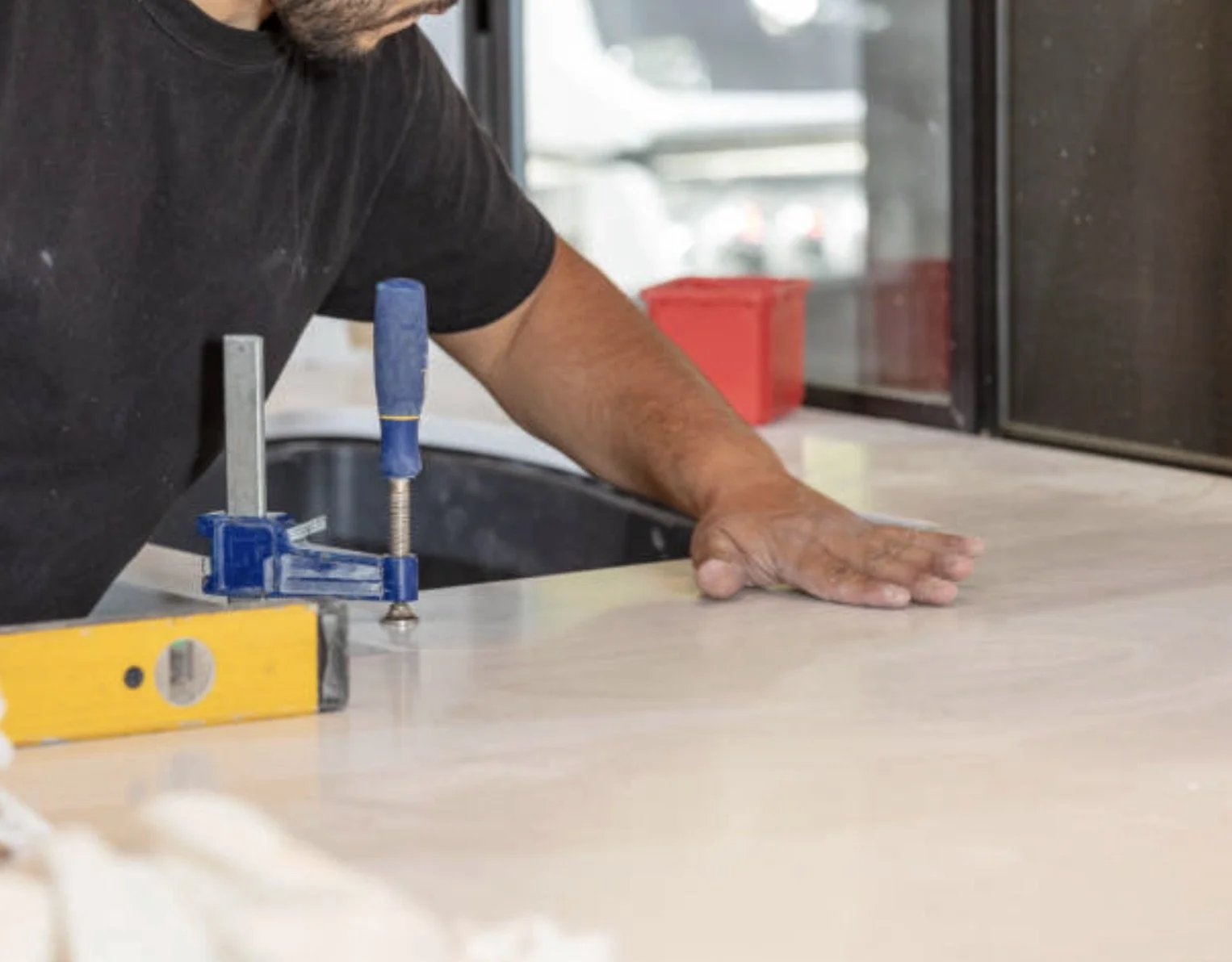 A person working on a kitchen countertop, using a clamp to hold a piece of material in place.