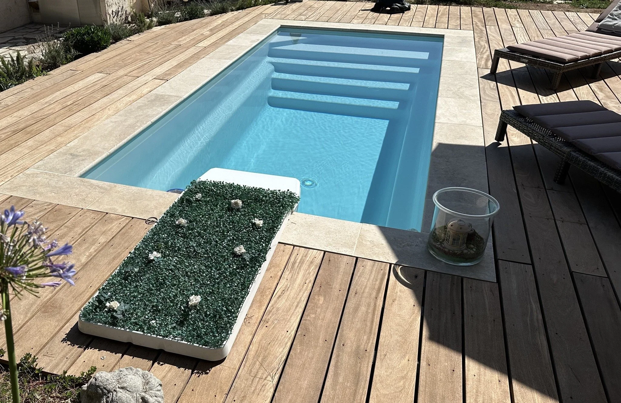 Piscine creusée dans une terrasse en bois avec deux chaises longues et une décoration avec une petite fontaine en verre.