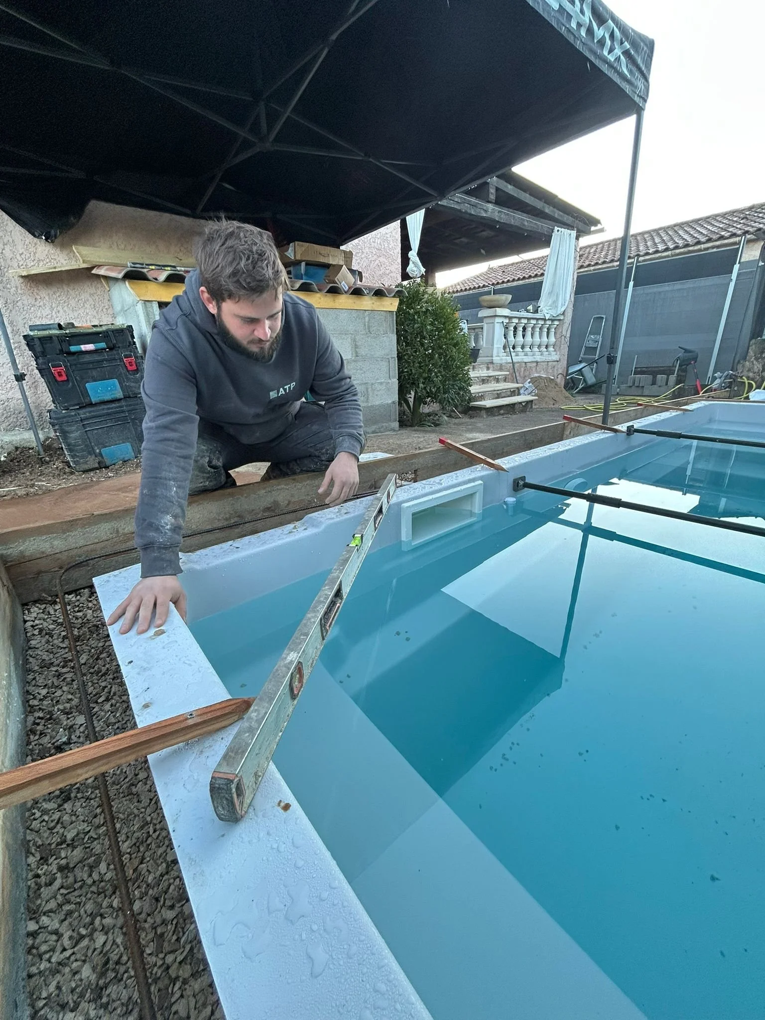 Un homme en train d'installer une piscine en construction, il regarde une règle à bulle placée sur le bord de la piscine.