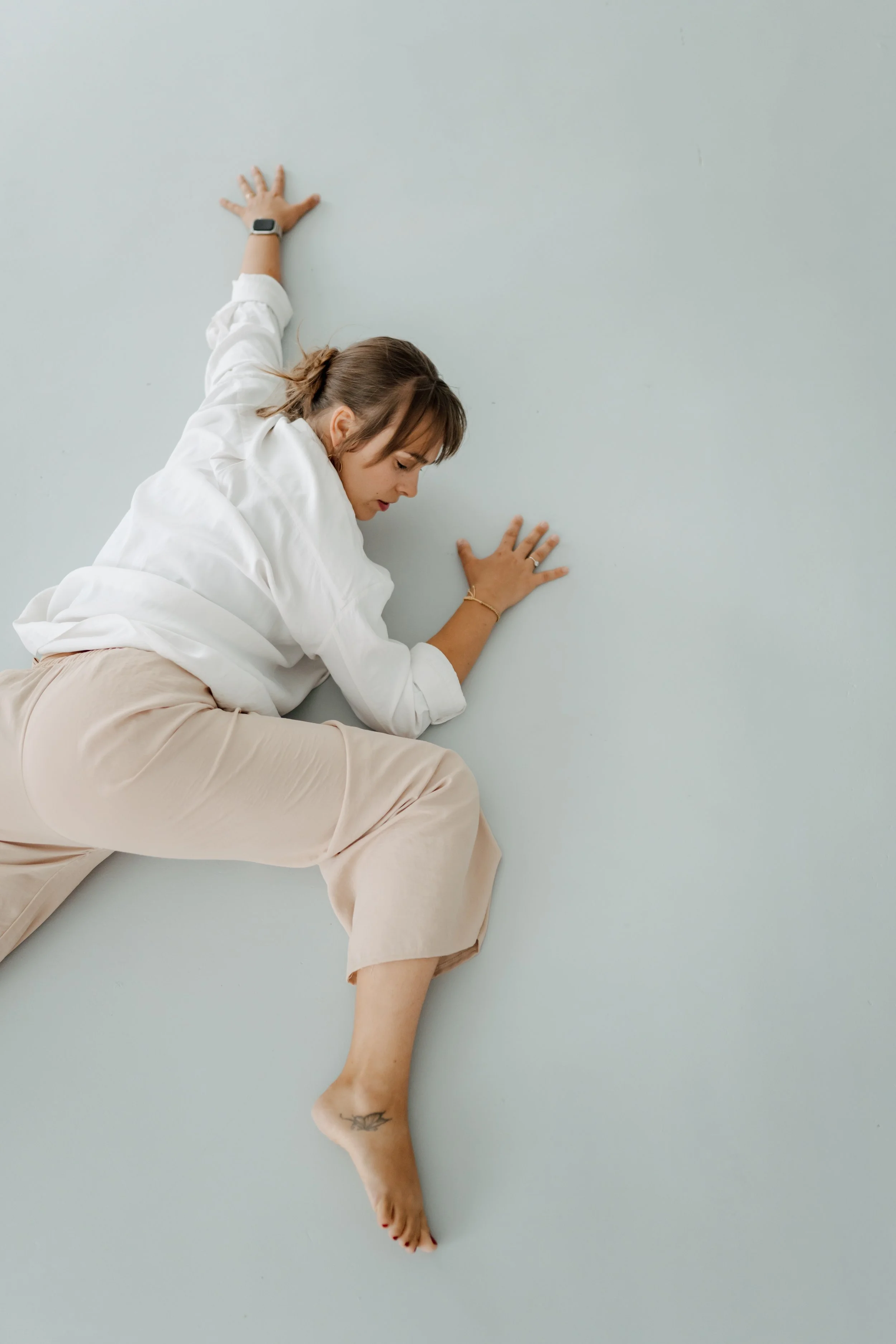 Woman resting on her side in a calm studio space, representing body-based therapeutic movement and Dance Movement Therapy focused on nervous system regulation and embodied awareness.
