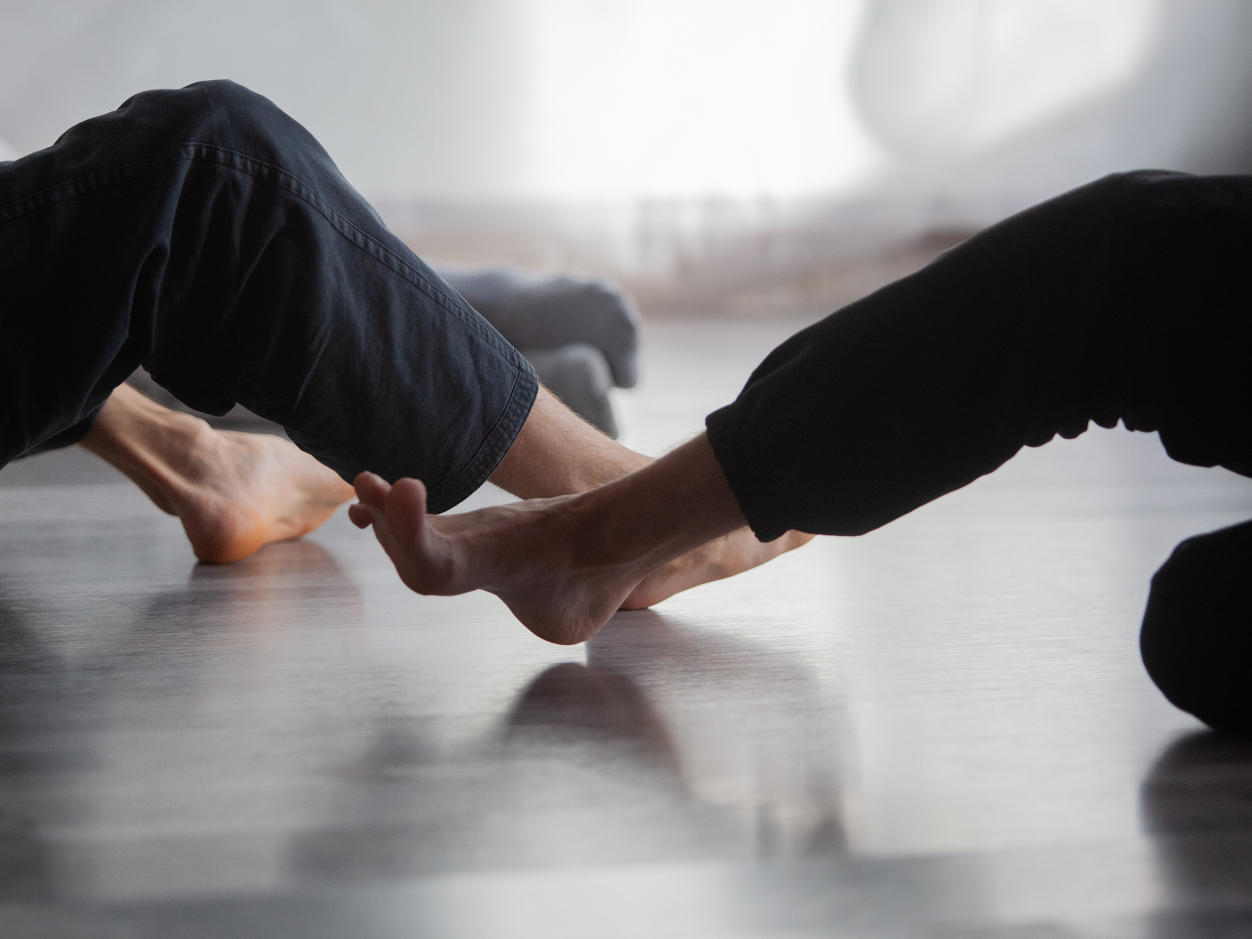 Two people practicing partner yoga, holding each other's feet while on the floor.