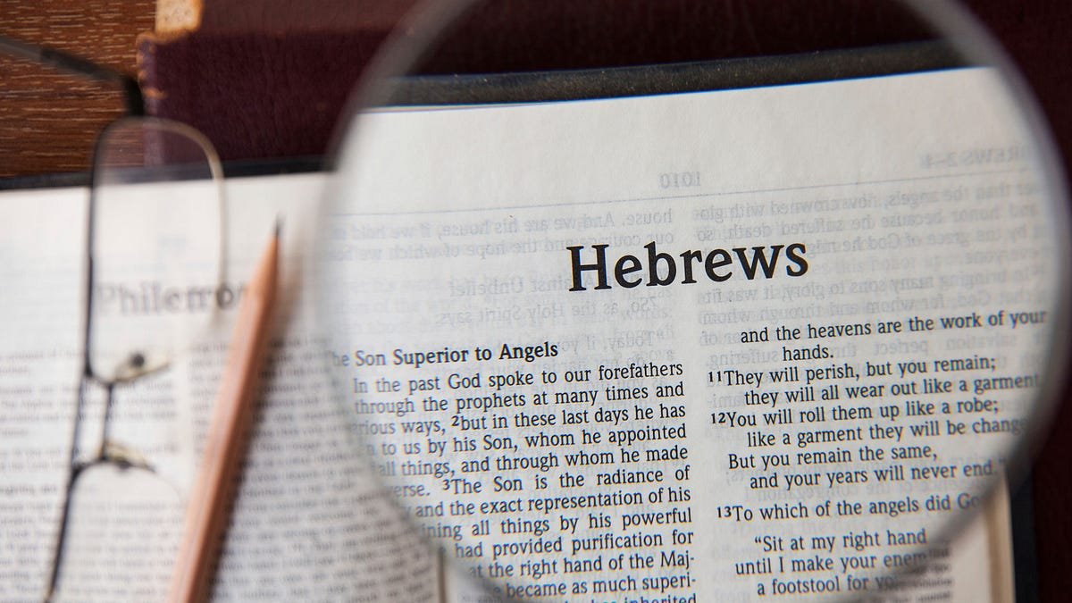 A magnifying glass focusing on a page of a Bible open to Hebrews, with the text visible through the glass.