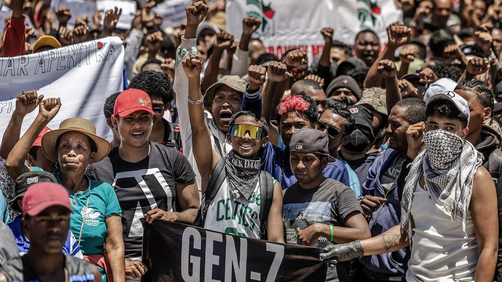 A large group of diverse protesters participating in a demonstration, many with raised fists, some holding banners and signs, expressing solidarity and activism.