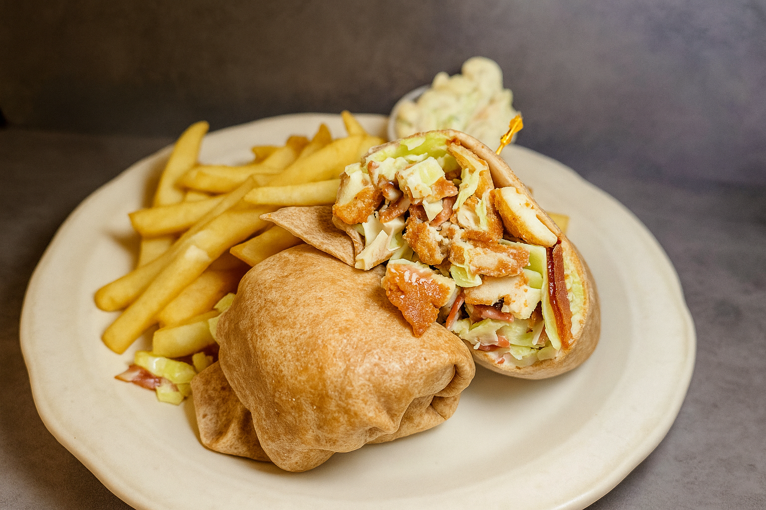 A plate with a chicken Caesar wrap, French fries, and a small side of coleslaw.