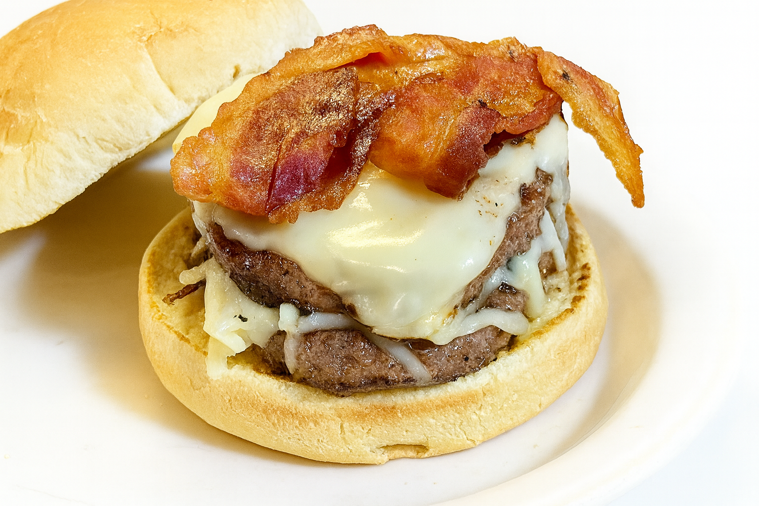 A bacon cheeseburger with a beef patty, melted cheese, a fried egg, and bacon on a sandwich bun, served on a white plate.