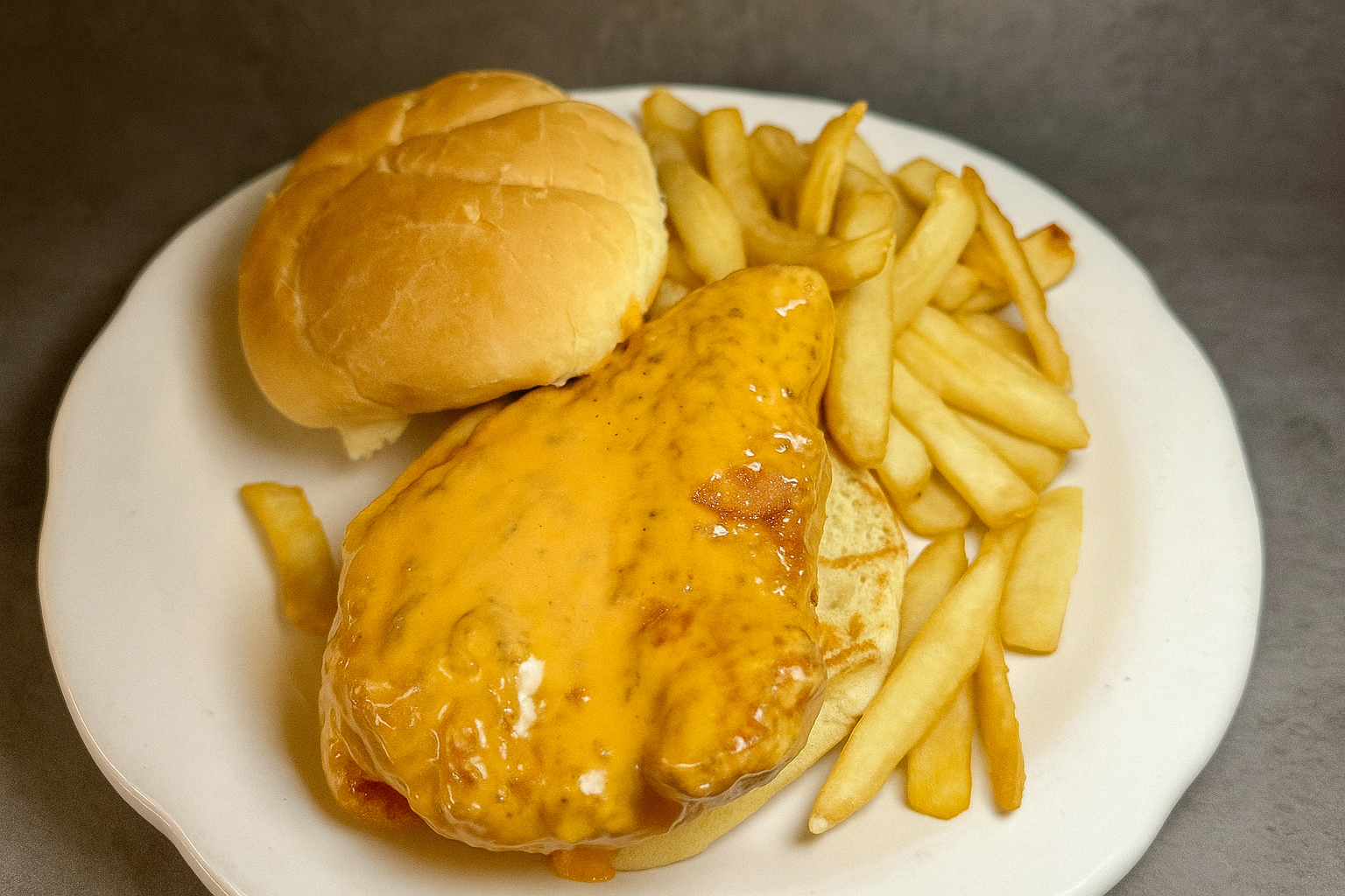 Plate of a fried chicken sandwich on a bun with buffalo hot sauce and served with French fries
