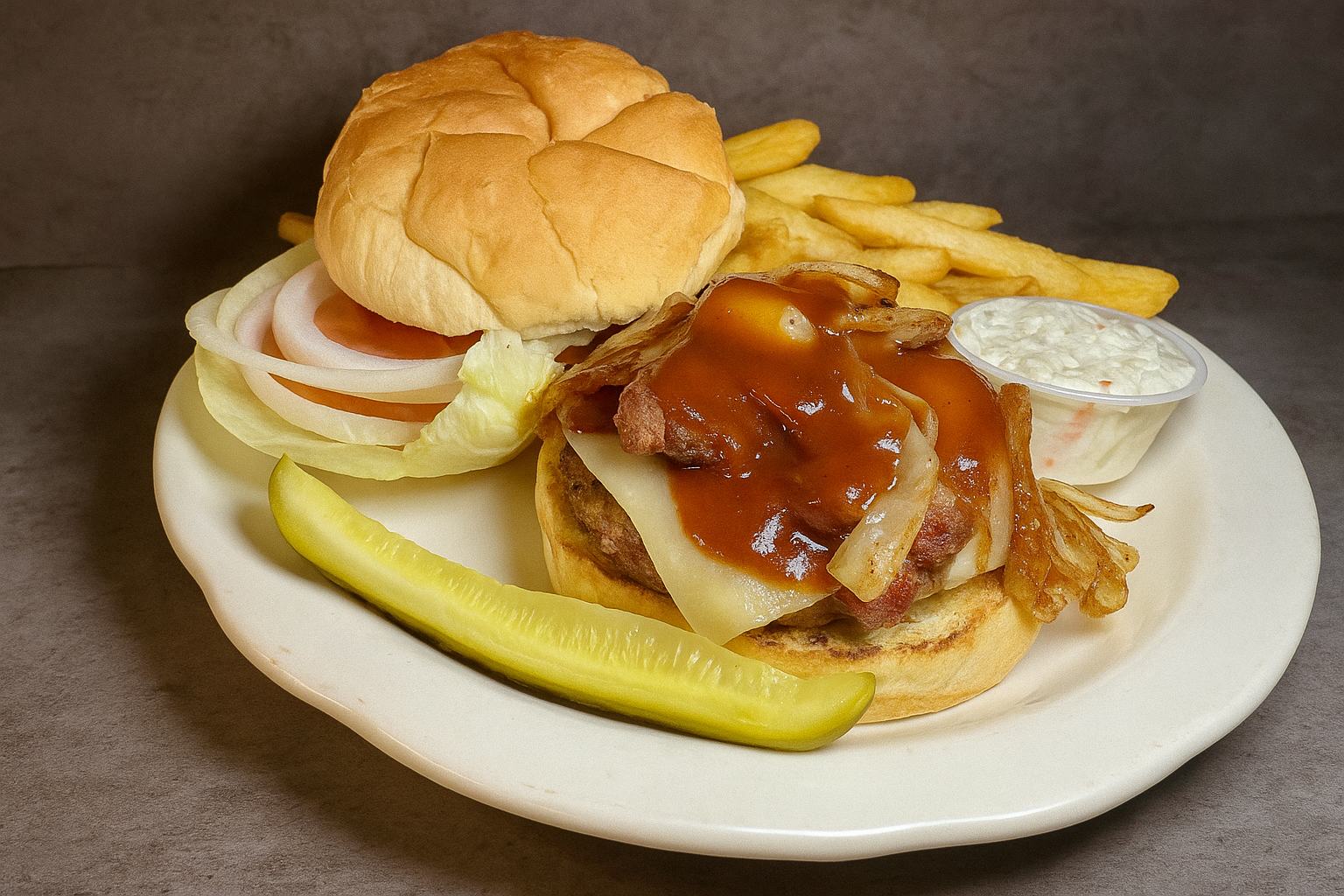 A plate of loose meat sandwich with bacon, cheese, onion, and gravy, paired with French fries, a dill pickle spear, a small cup of cottage cheese, and a sandwich bun.