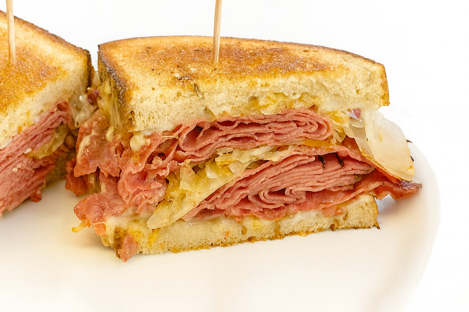Cross-section of a ham and cheese grilled sandwich on white plate, showing layers of ham, melted cheese, and toasted bread.