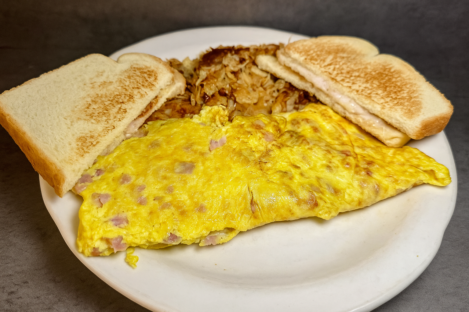 Plate with scrambled egg omelette, with two slices of toasted bread, and cooked hash browns.